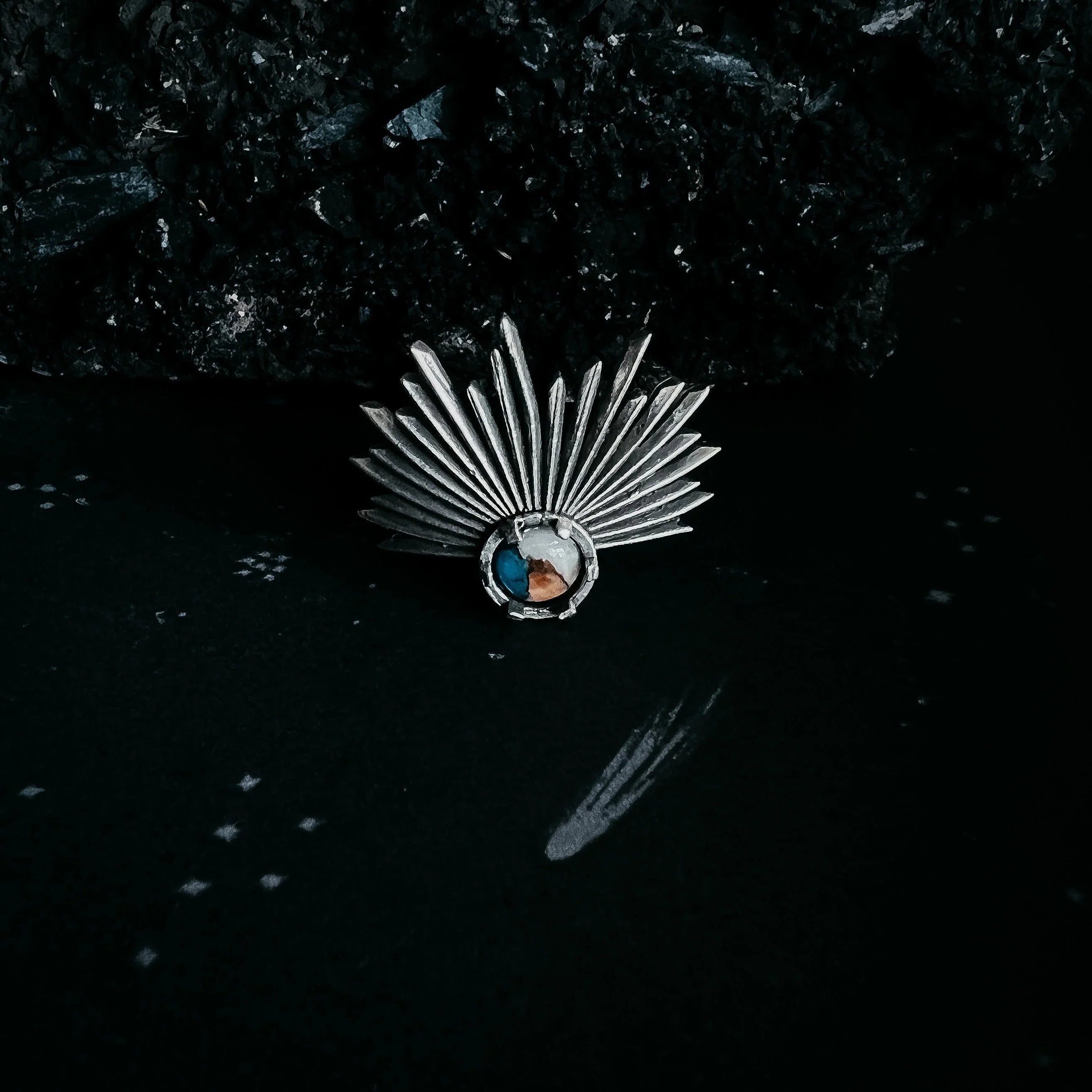 Silver metal brooch with fan-shaped spikes and a round centerpiece on a dark reflective surface