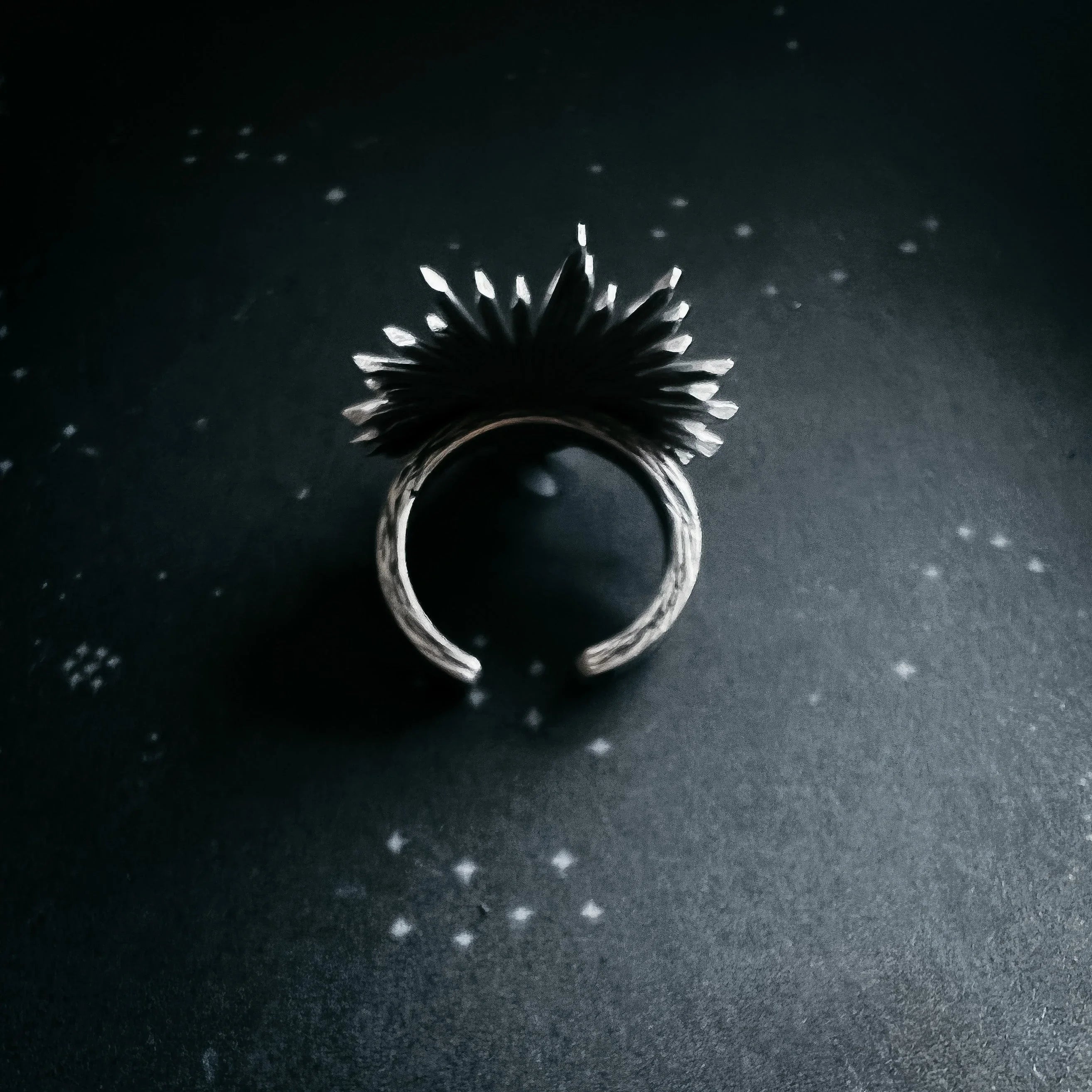 silver adjustable ring with black feather-like design casting shadows on dark surface