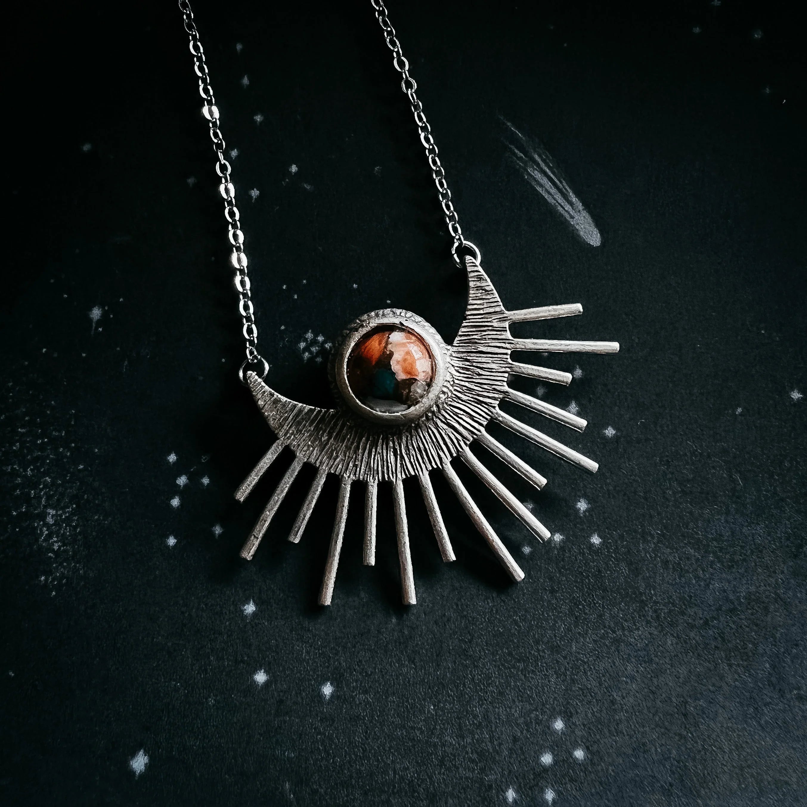 Silver necklace with sunburst pendant featuring a round brown gemstone on a dark starry background