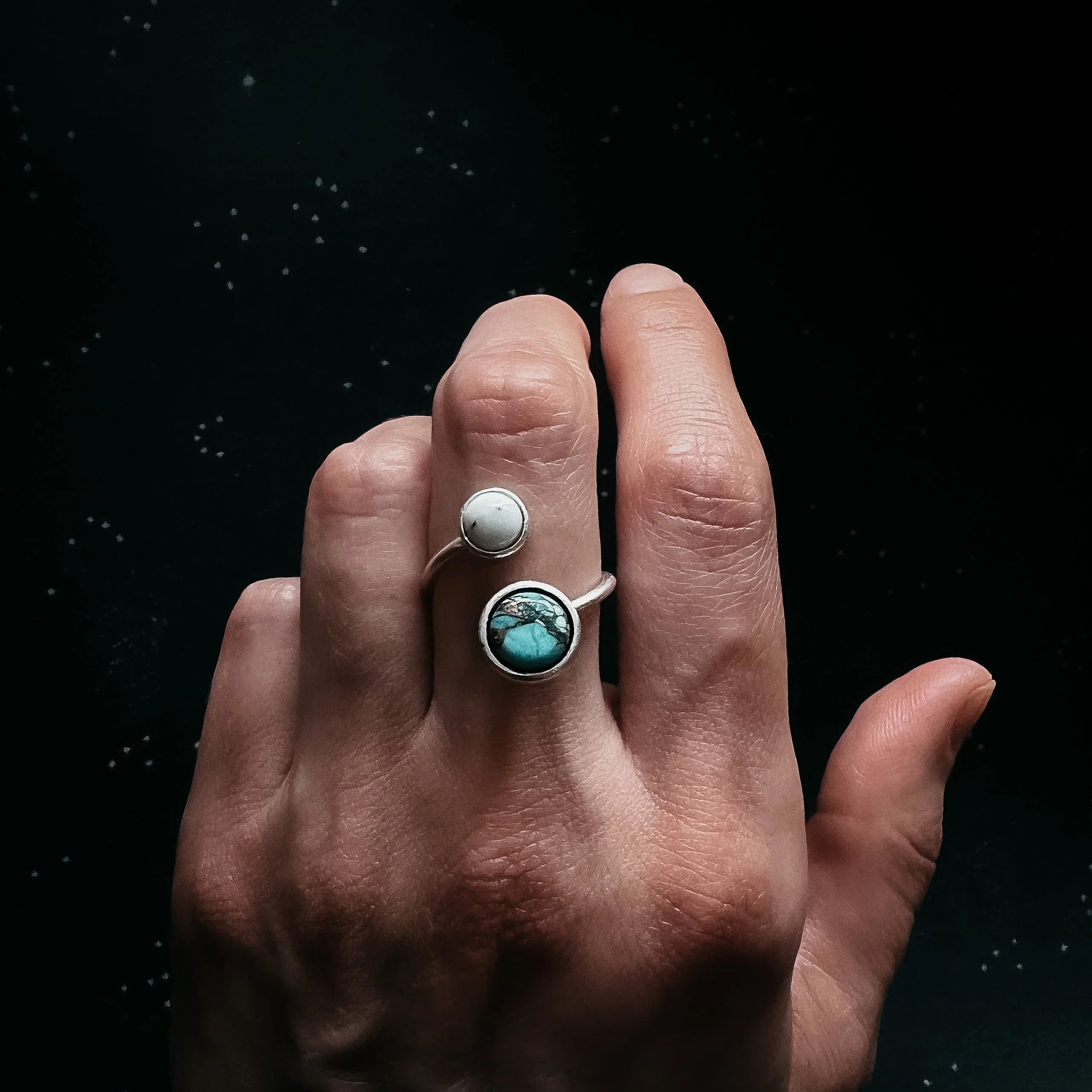 Hand wearing silver open ring with white and turquoise stones on black background