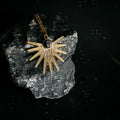 gold starburst pendant necklace with blue stone on dark textured rock and starry background