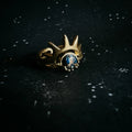 Gold ring with blue gemstone and cosmic crown design on a star-speckled black surface