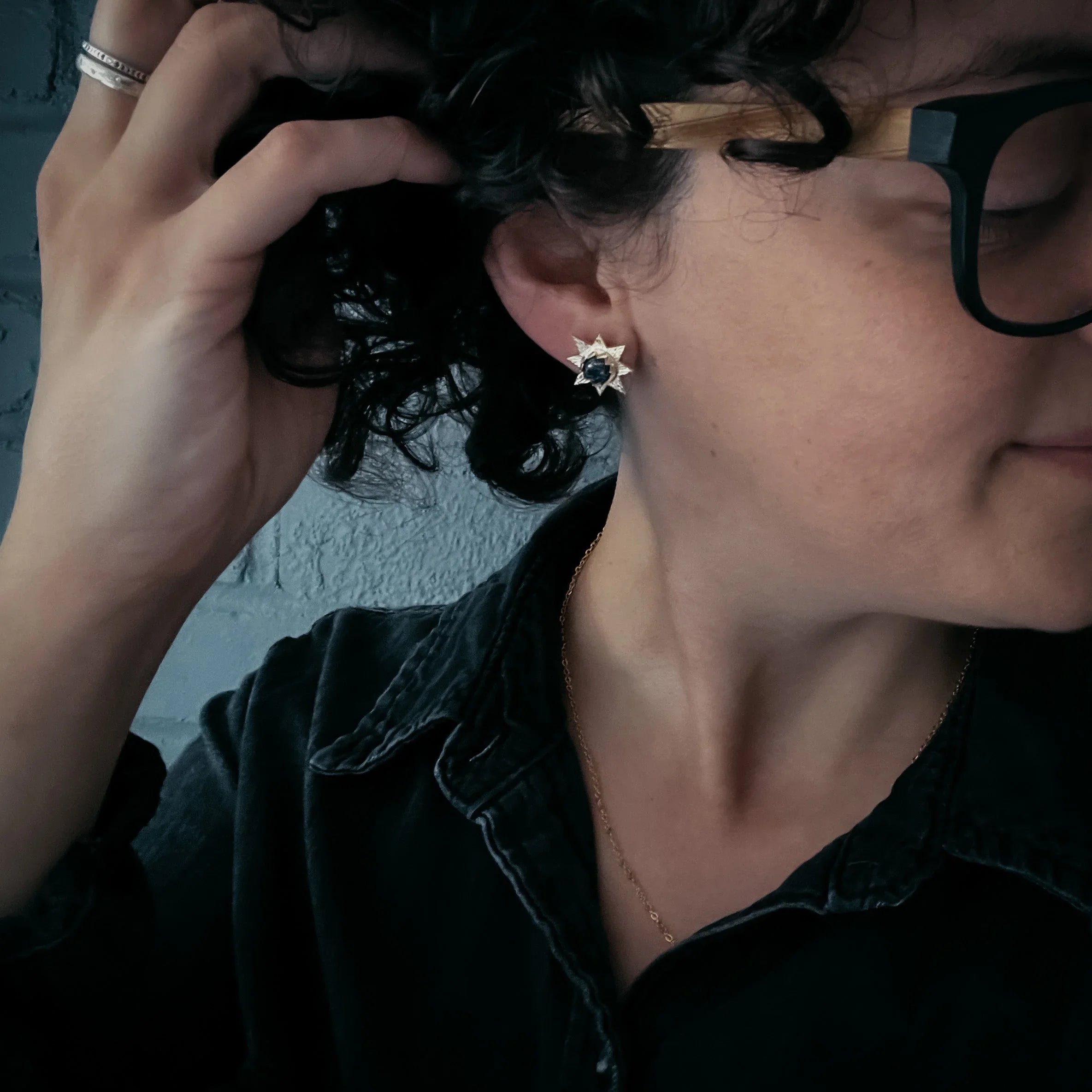 Woman wearing cosmic star-shaped earring, black glasses, and dark collared shirt at Qu!rk Boutique