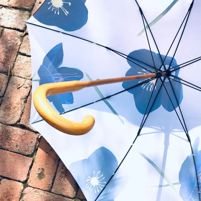 White umbrella with blue floral pattern and curved wooden handle on brick pavement
