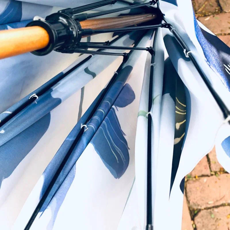 Close-up of the frame and spoke structure of a blue and white floral patterned umbrella on a brick surface