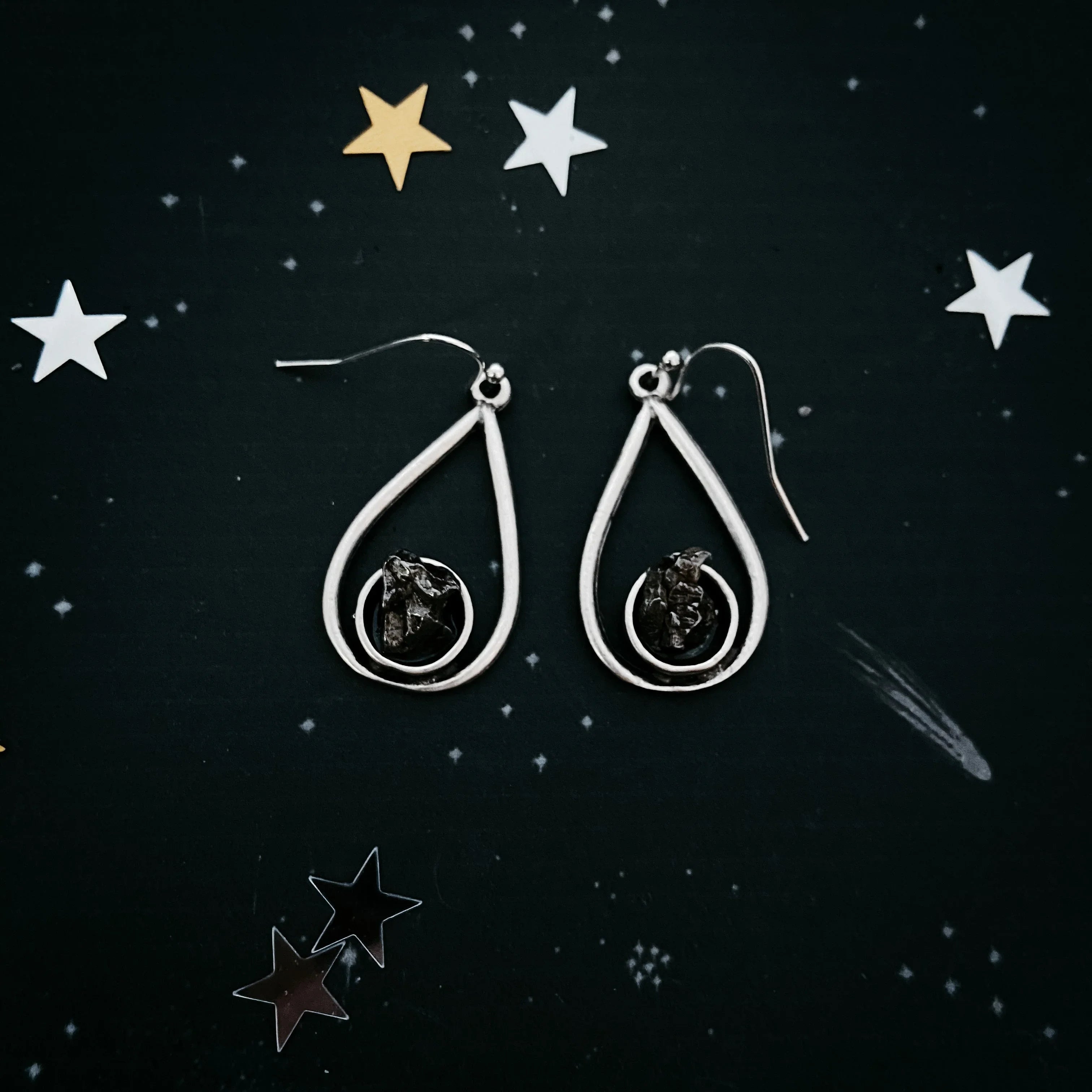 Silver teardrop earrings with dark irregular stones on black starry background