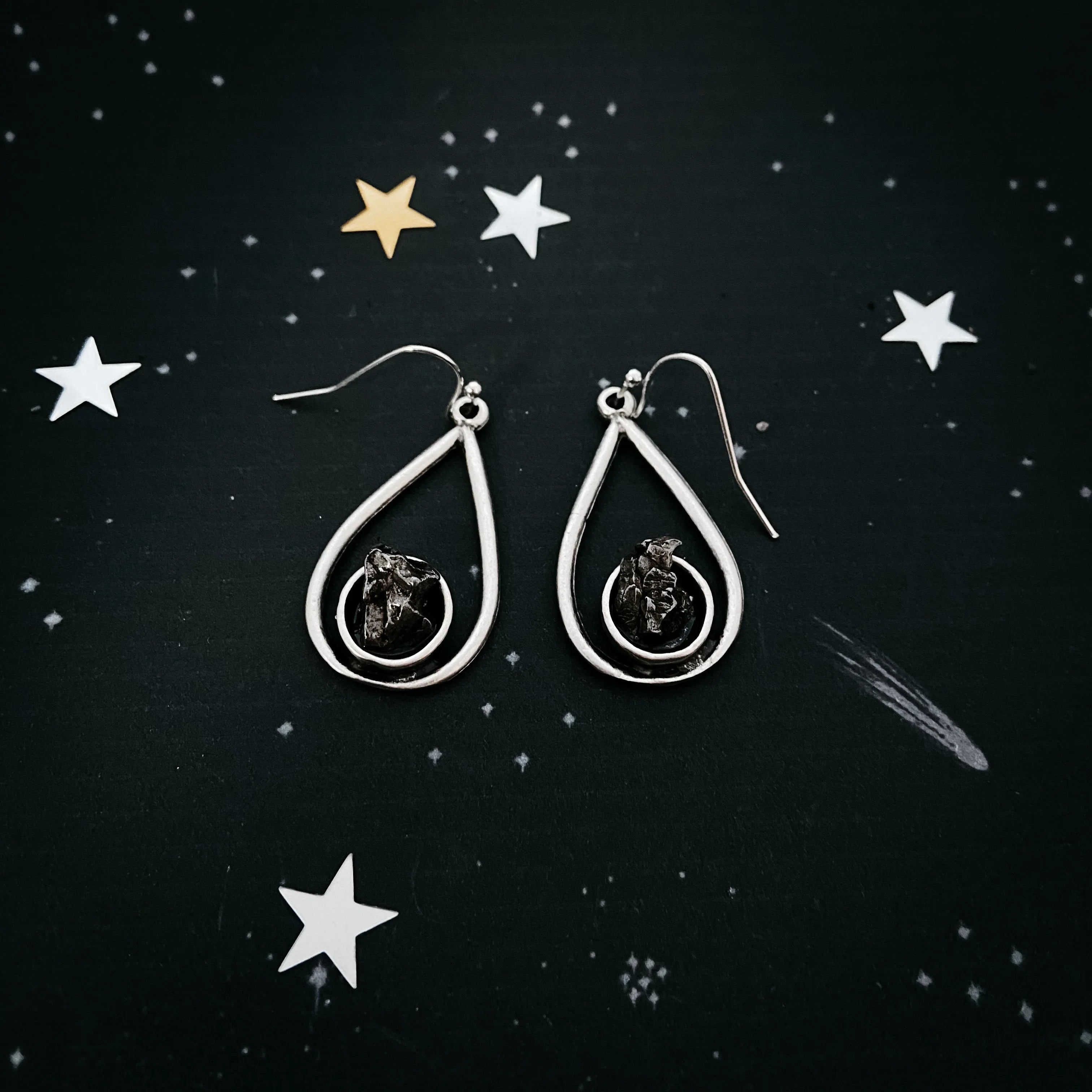 Silver teardrop earrings with black raw stone centers on starry black background