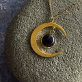 Gold crescent moon necklace with cosmic black stone pendant on textured gray surface