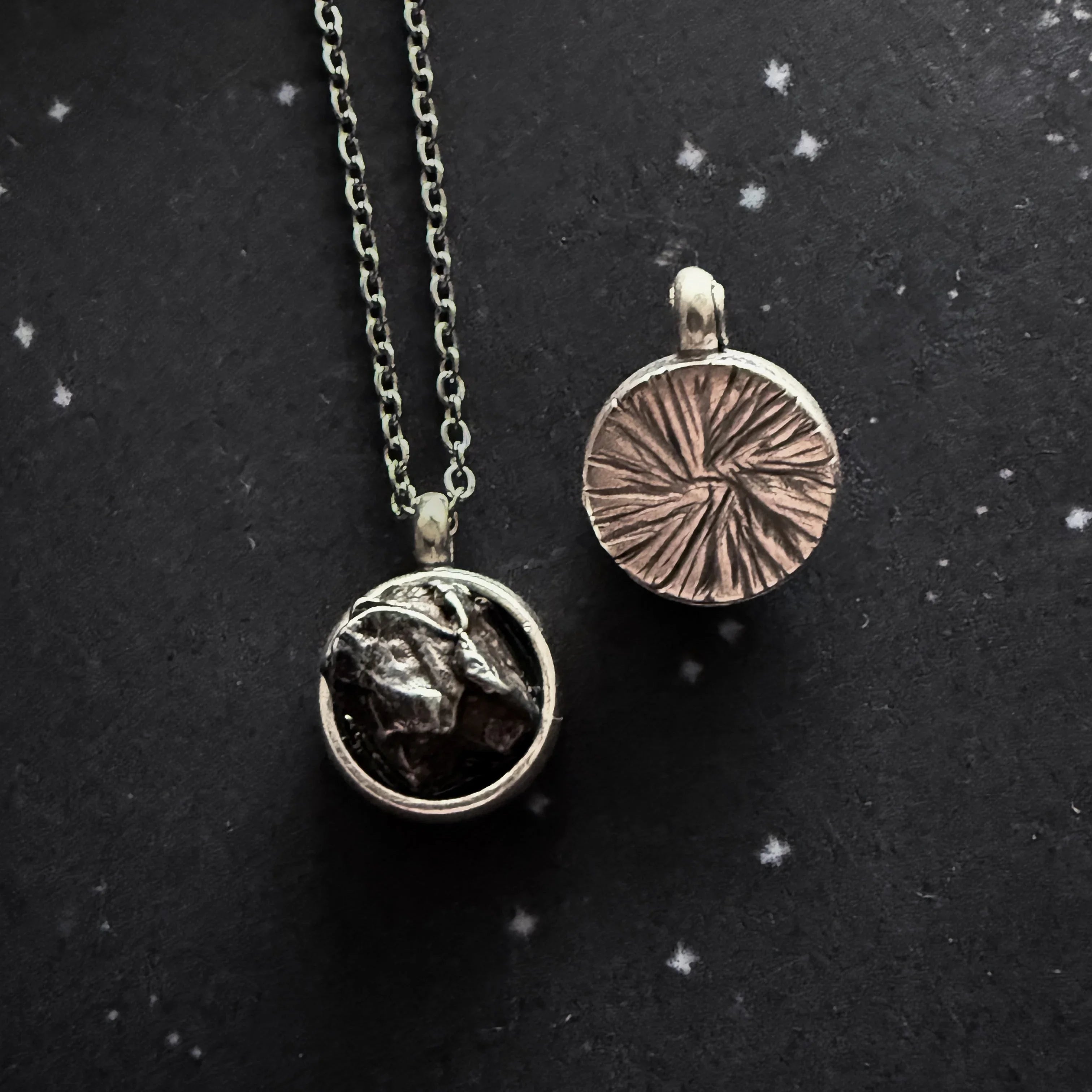 Silver necklace and pendant with meteorite fragments and textured design on black starry background