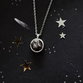 Silver necklace with rough dark stone pendant on black starry background with gold and silver star decorations