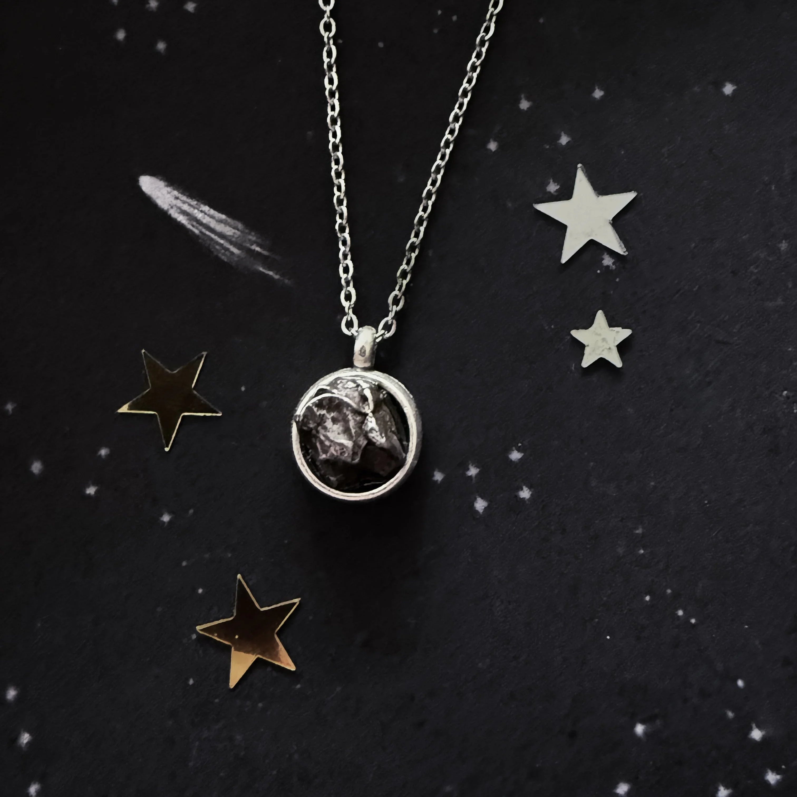 Silver necklace with rough dark stone pendant on black starry background with gold and silver star decorations