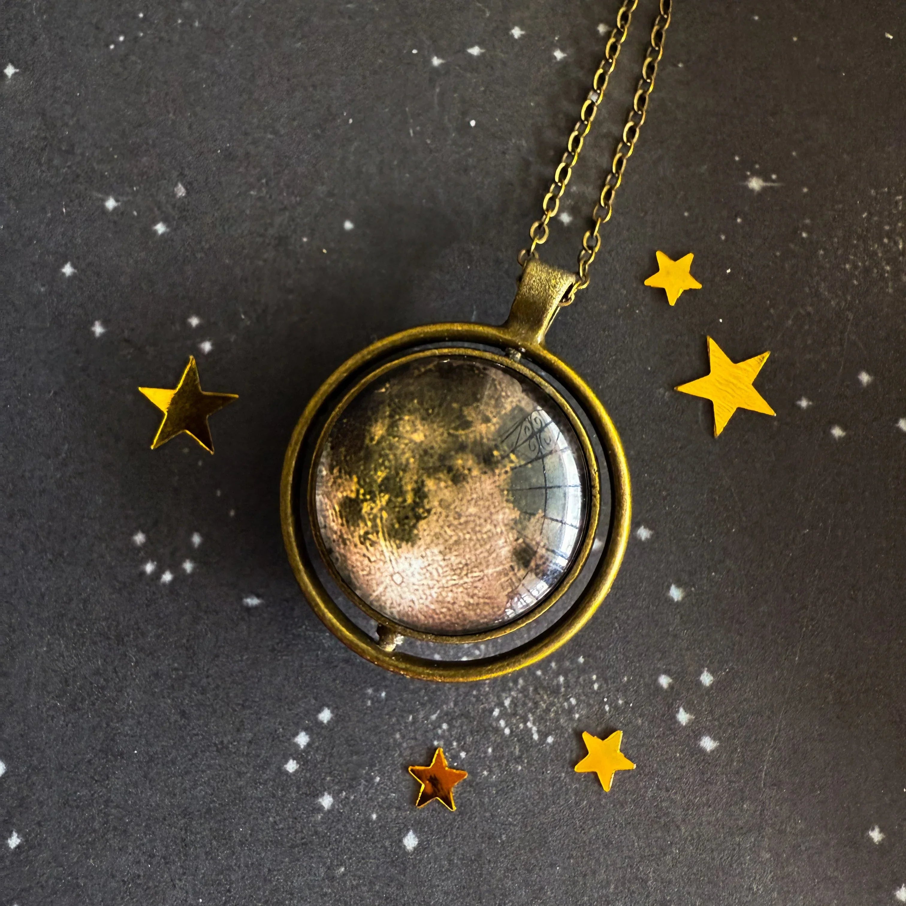 Cosmic-themed pendant necklace with bronze finish, surrounded by gold stars on a dark starry background.