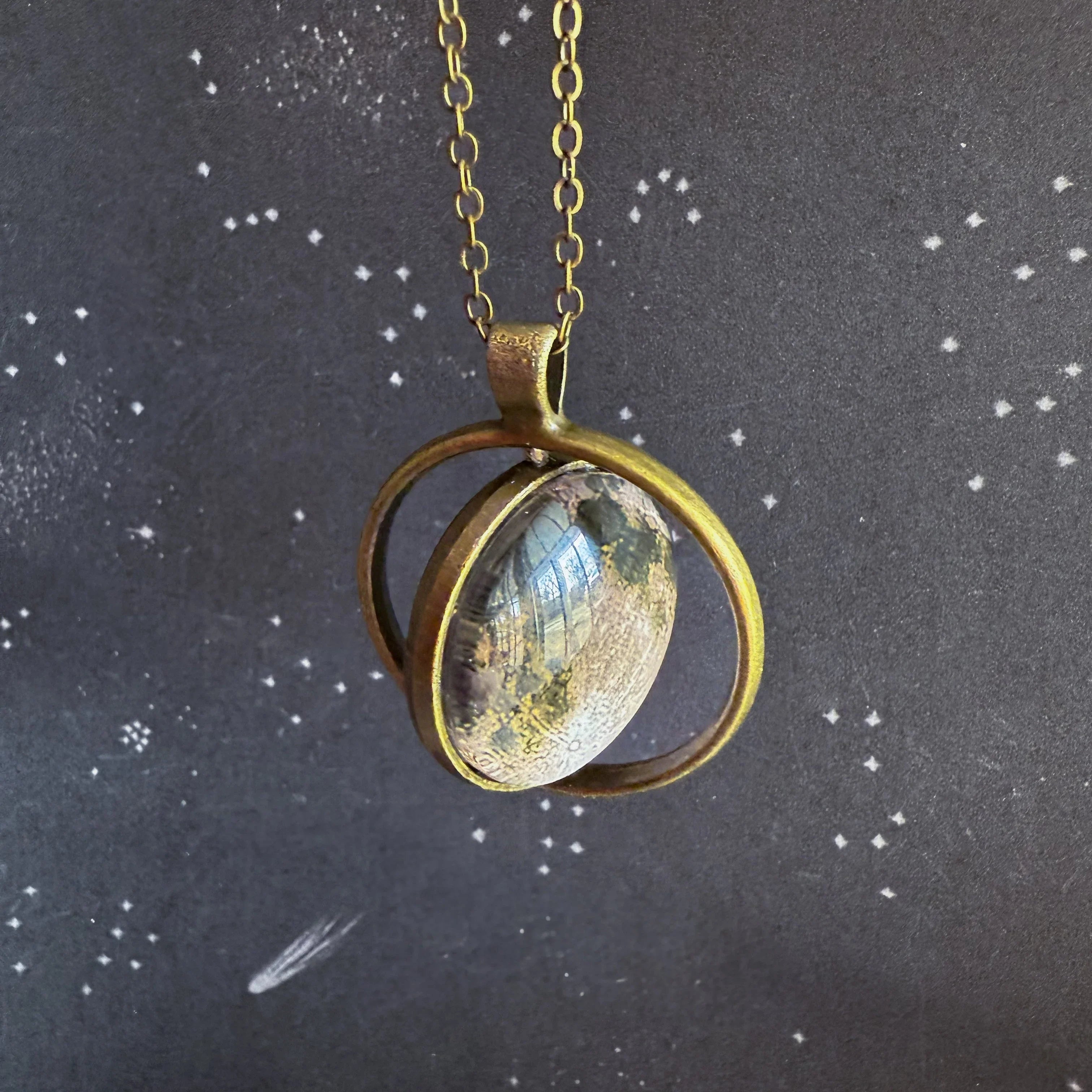 Artist-designed brass pendant necklace with glass cabochon on cosmic star background