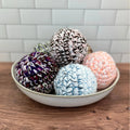 Colorful handmade crochet bath puffs in a ceramic bowl, Qu!rk Boutique gift shop display