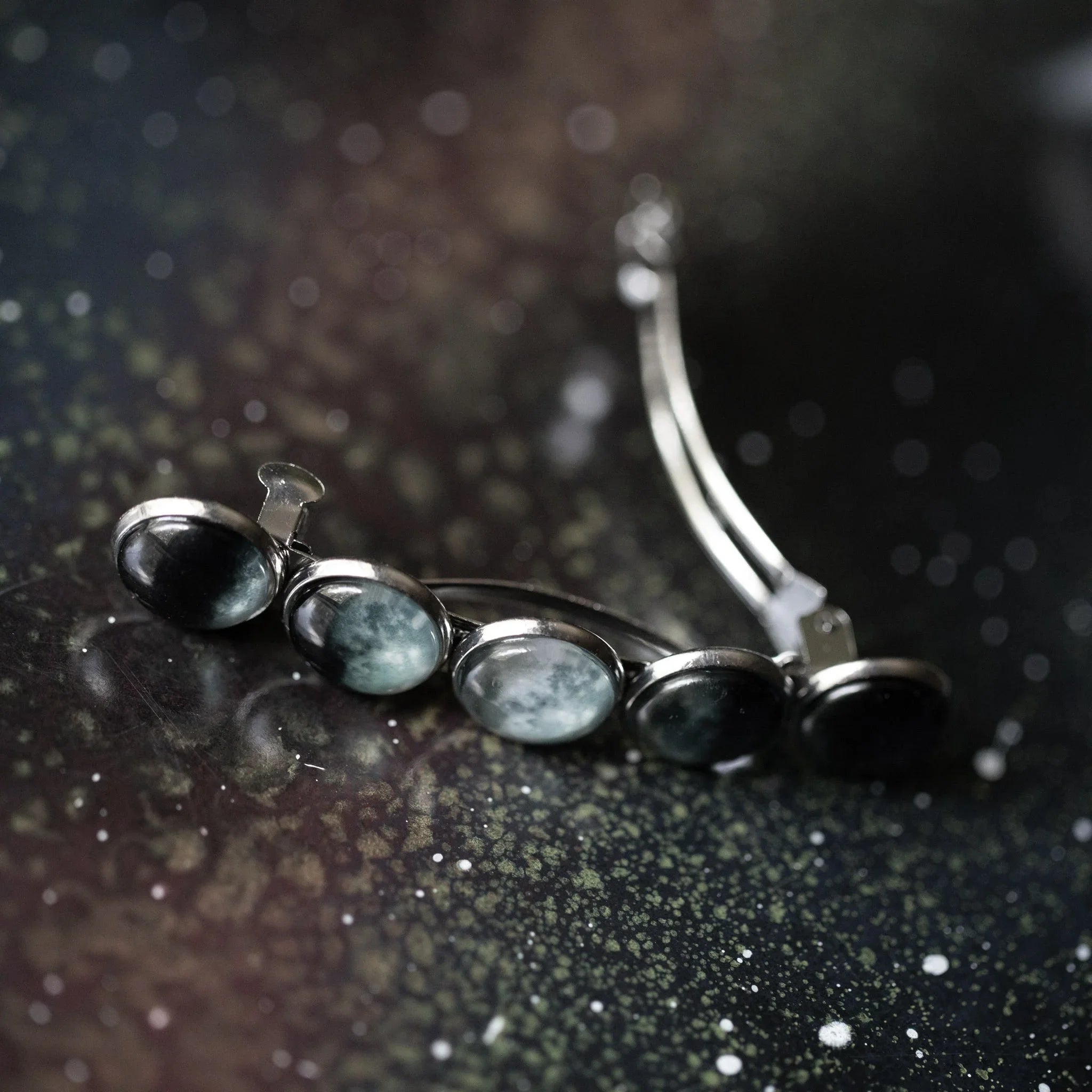 Silver hair clip with five round moon phase stones on speckled dark surface