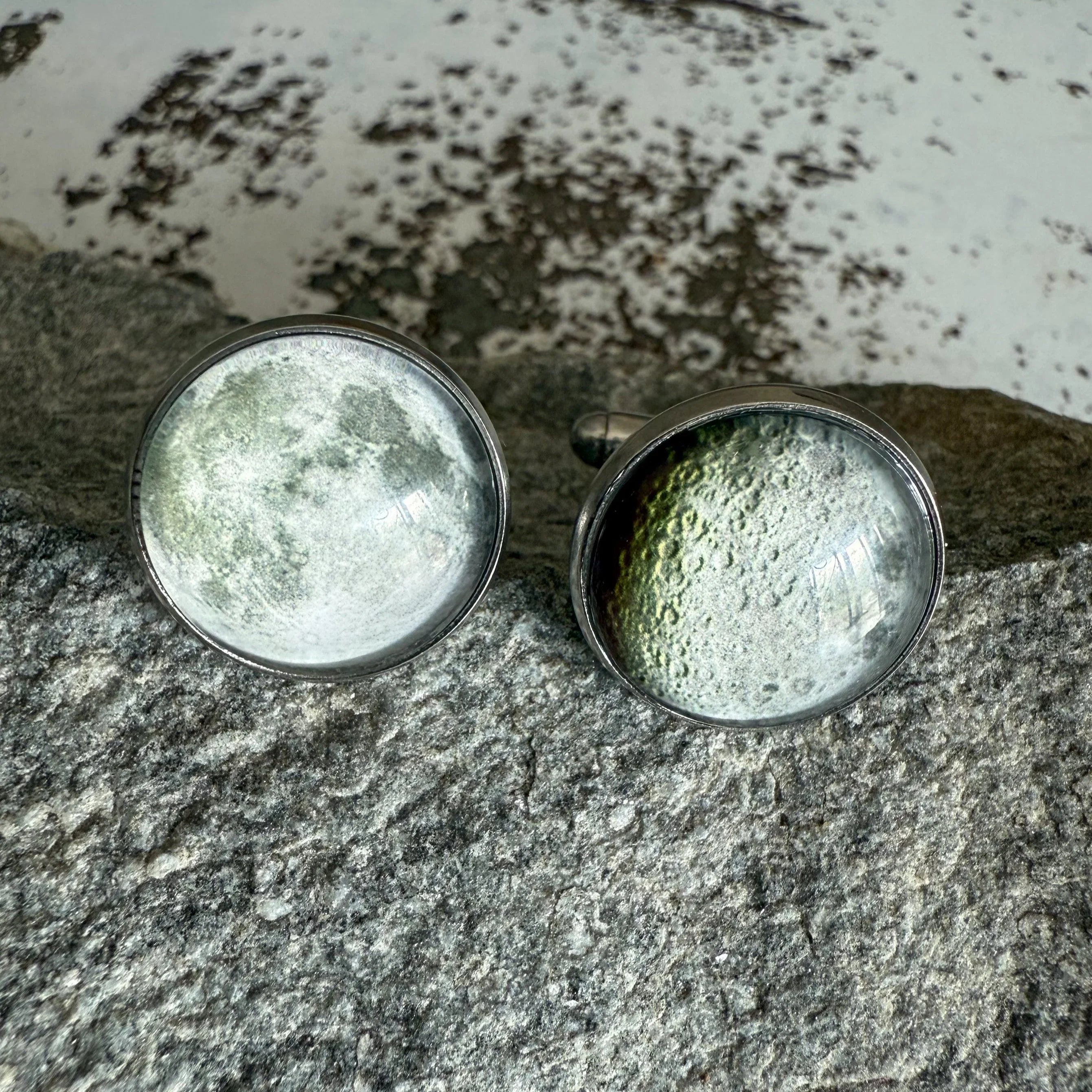 Pair of round cufflinks with detailed moon surface design on gray stone background