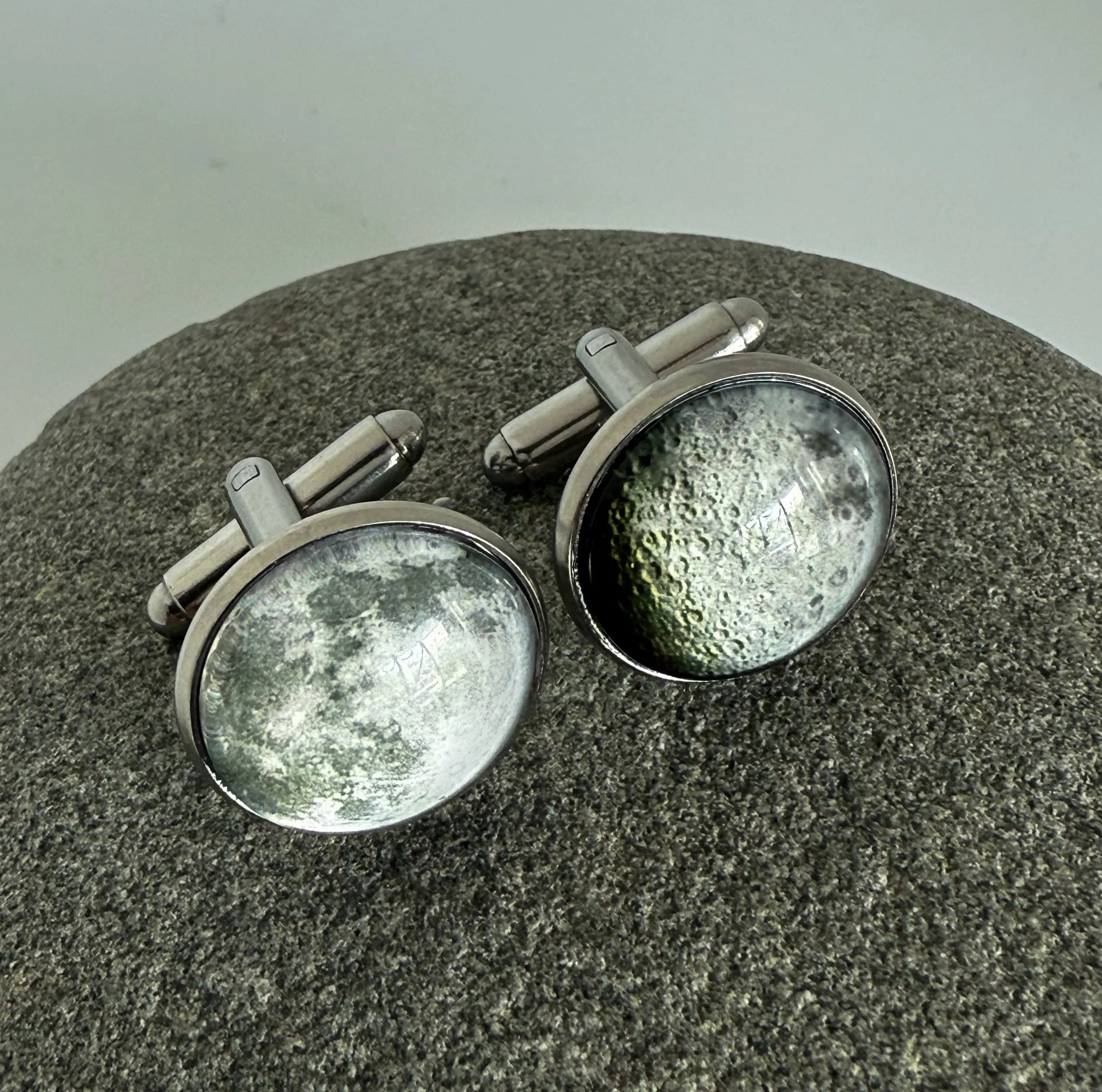 Silver cufflinks with moon surface design resting on textured gray stone