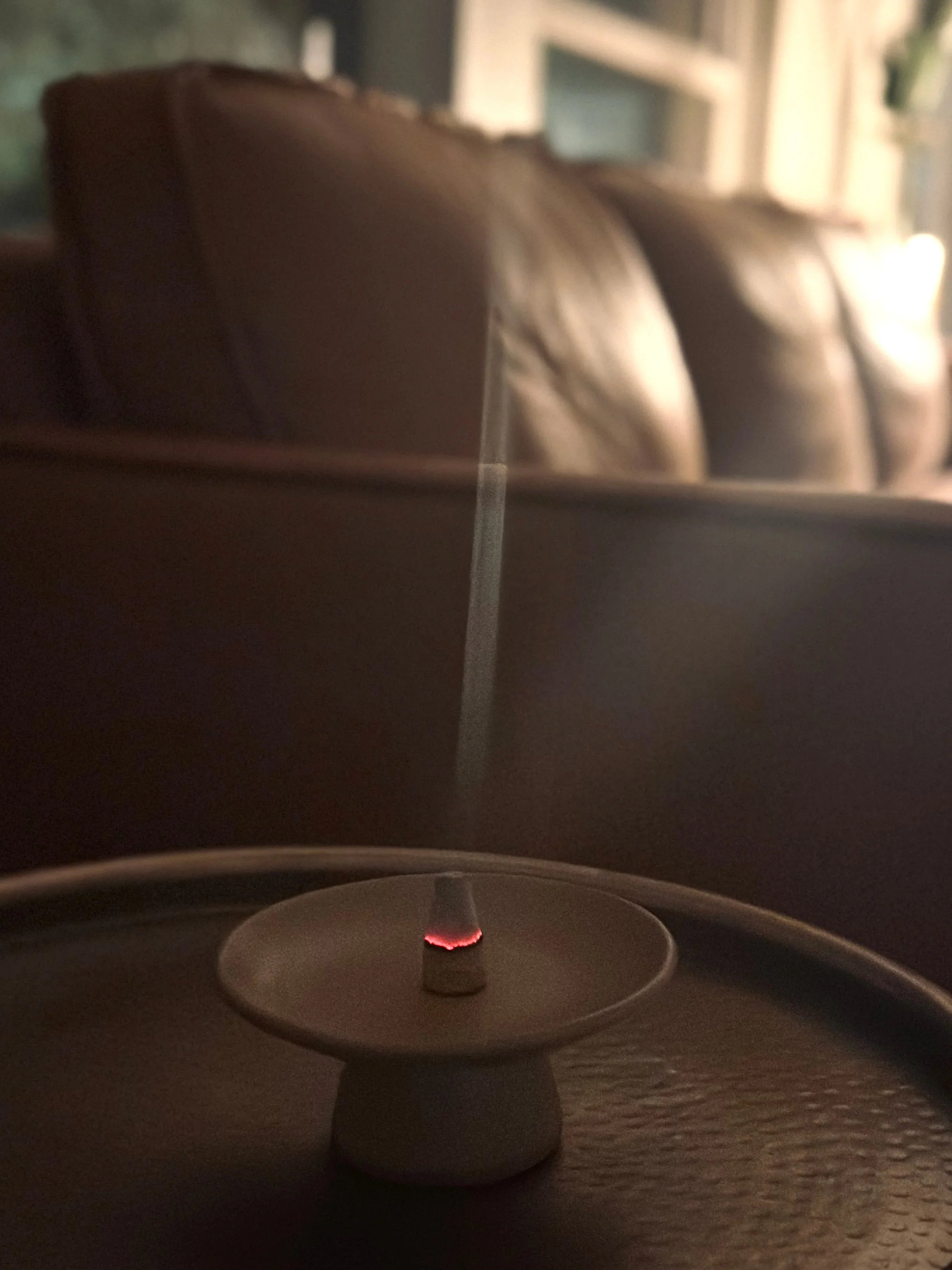 Incense cone burning on a ceramic holder with smoke rising, cozy living room background