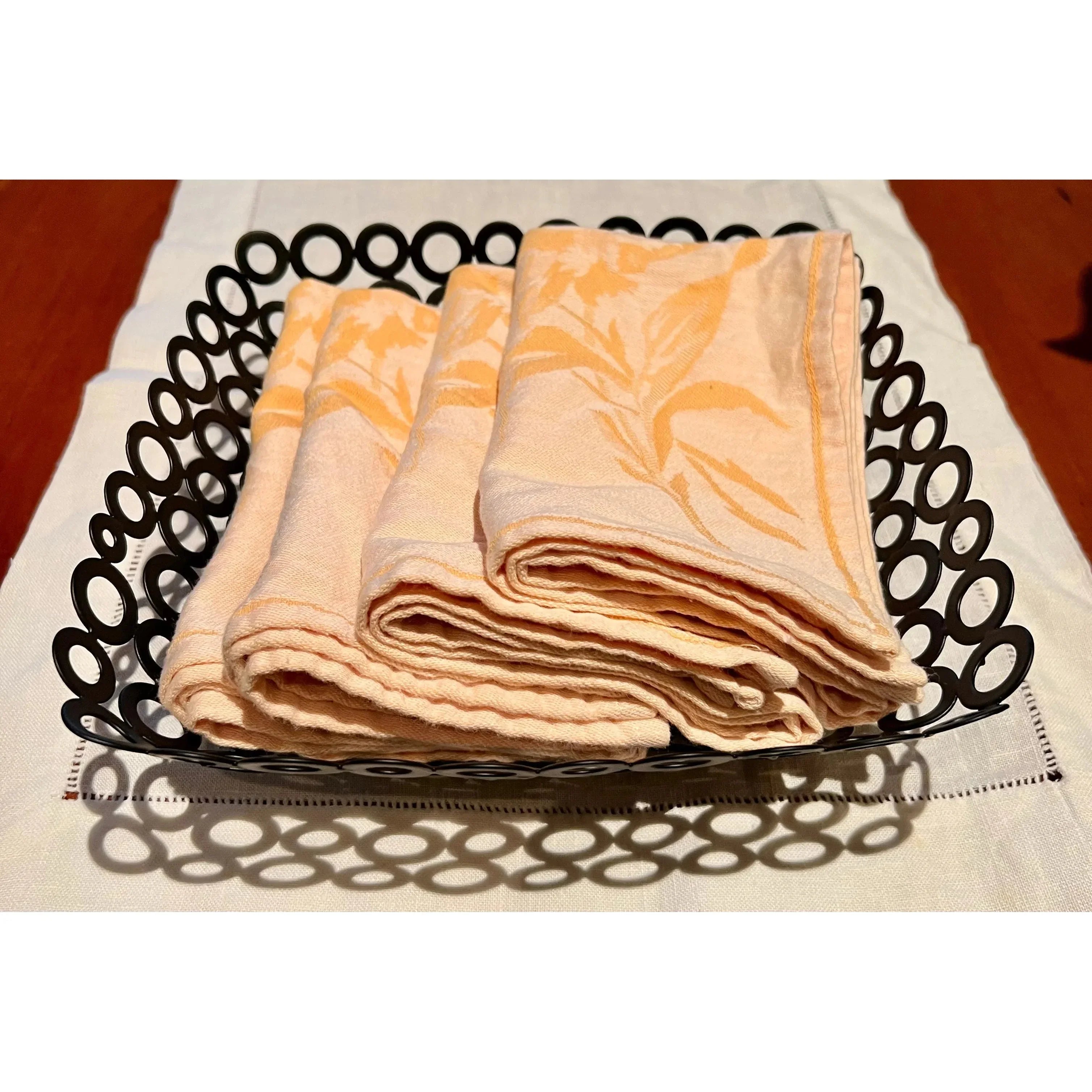 Folded peach patterned cloth napkins in a decorative black metal basket on a table runner