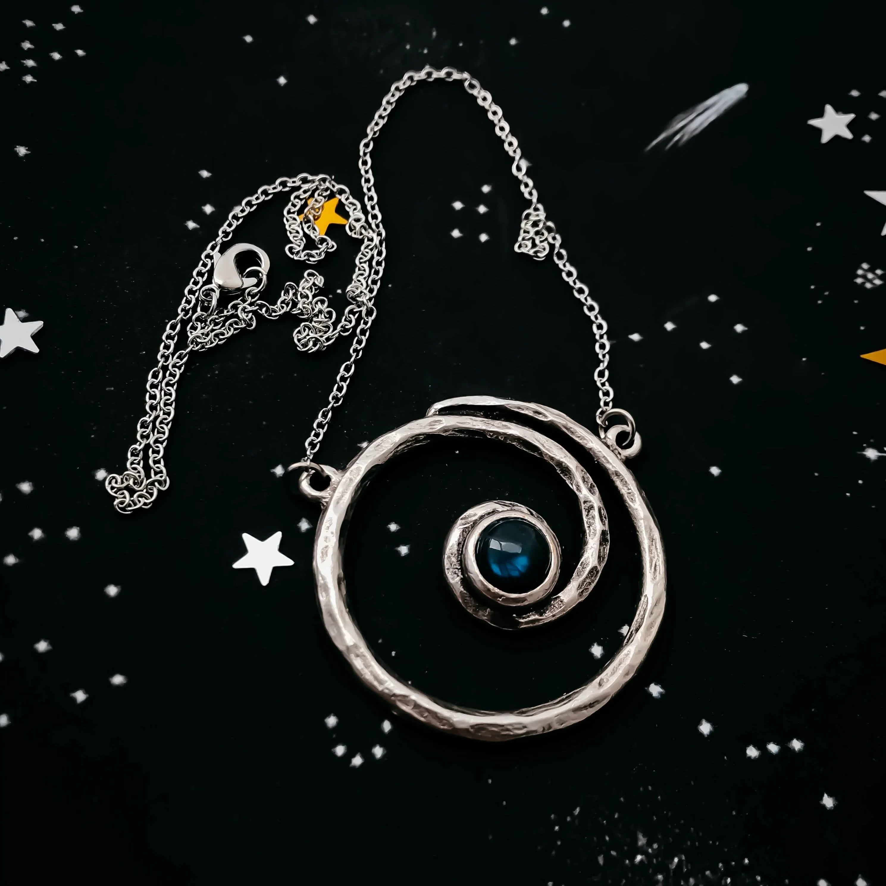 Cosmic spiral silver necklace with blue stone on starry background, Qu!rk Boutique jewelry