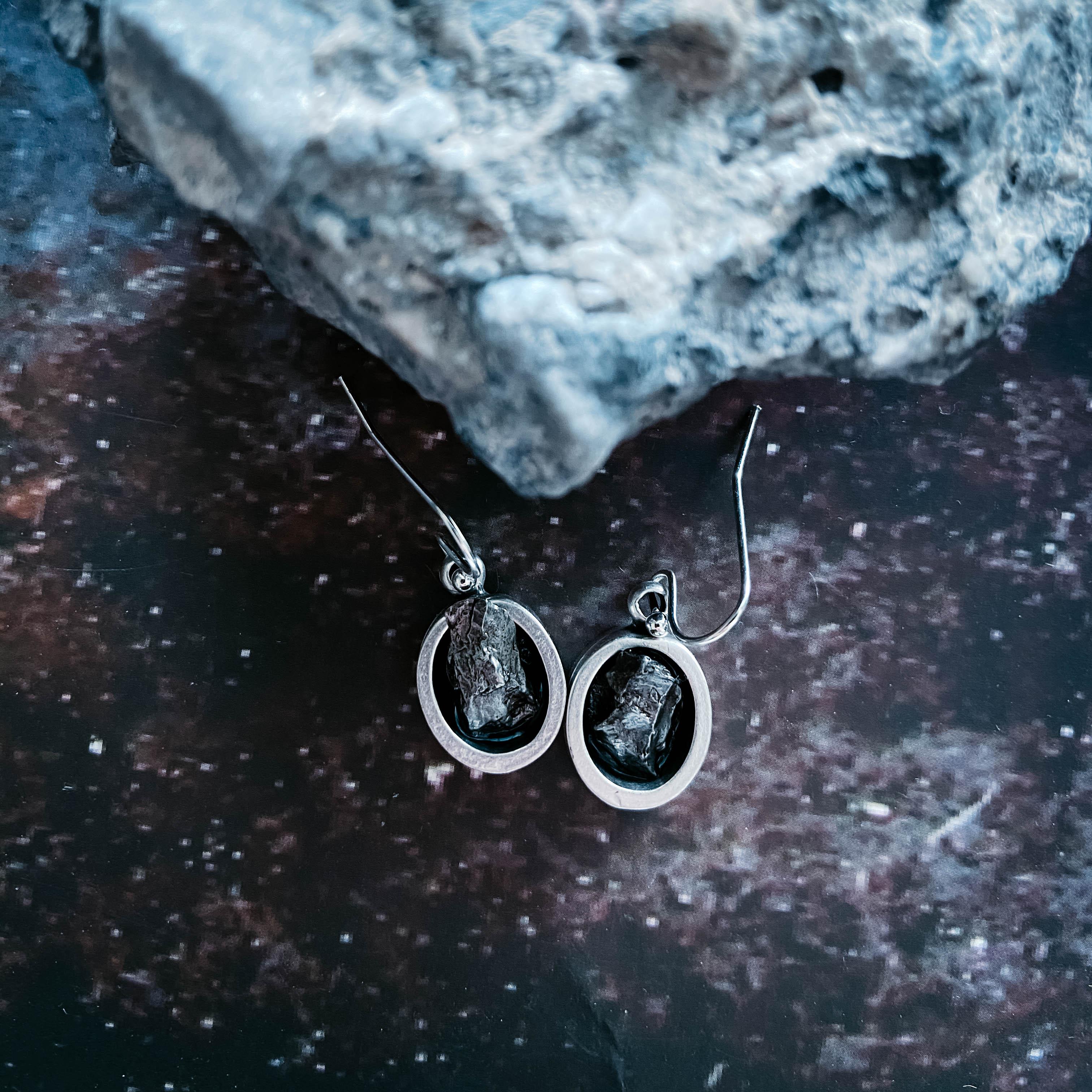 Raw stone cosmic earrings in silver oval setting, styled on a space-inspired background