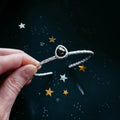 Hand holding hammered silver bangle with black stone against starry dark background