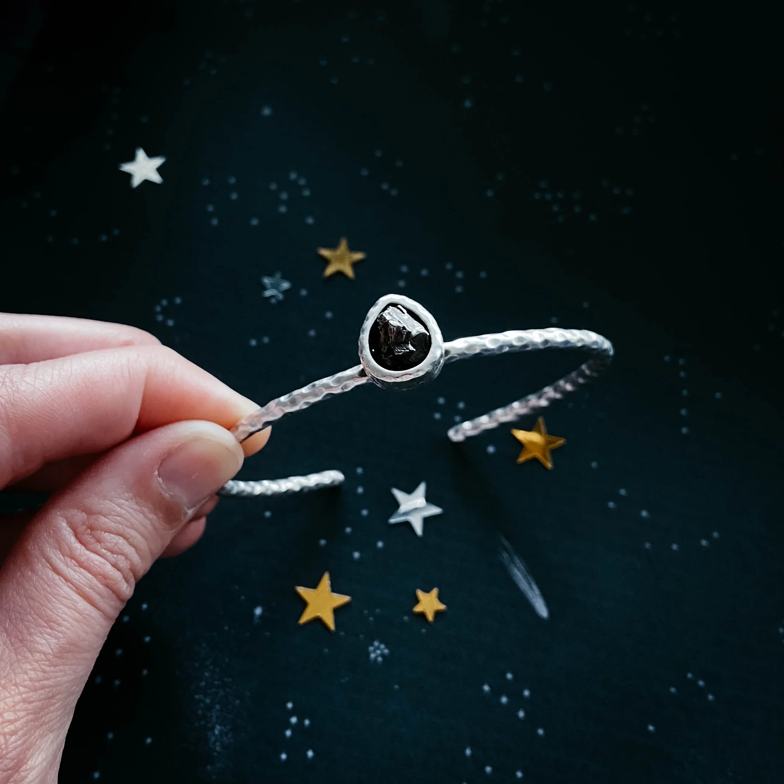 Hand holding hammered silver bangle with black stone against starry dark background