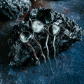 Three silver hairpins with moon phase glass cabochons on porous black volcanic rock