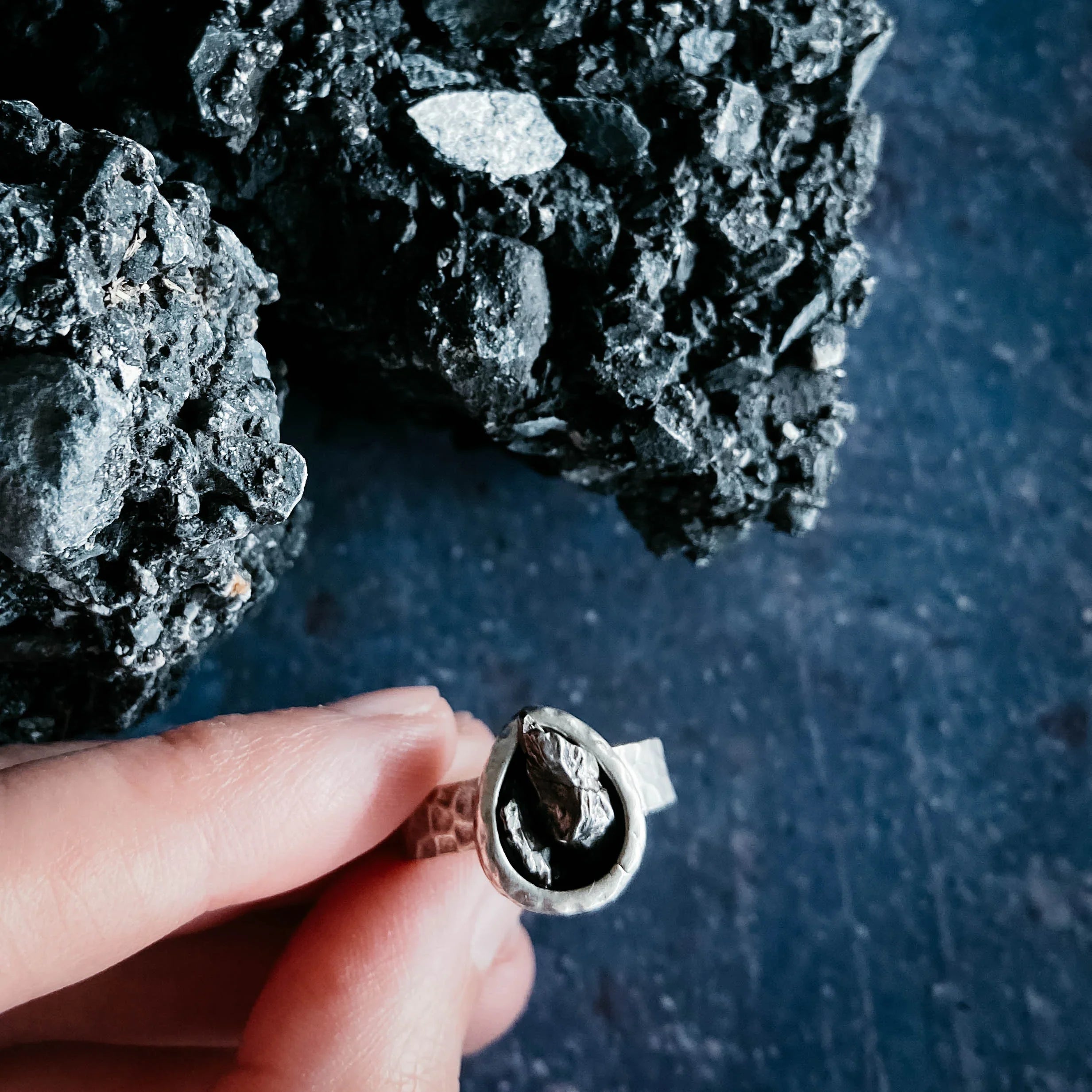 Hand holding silver artisan ring with raw stone, against black mineral background, Qu!rk Boutique