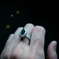 Hand wearing a hammered silver ring with a dark stone, cosmic star background, Qu!rk Boutique