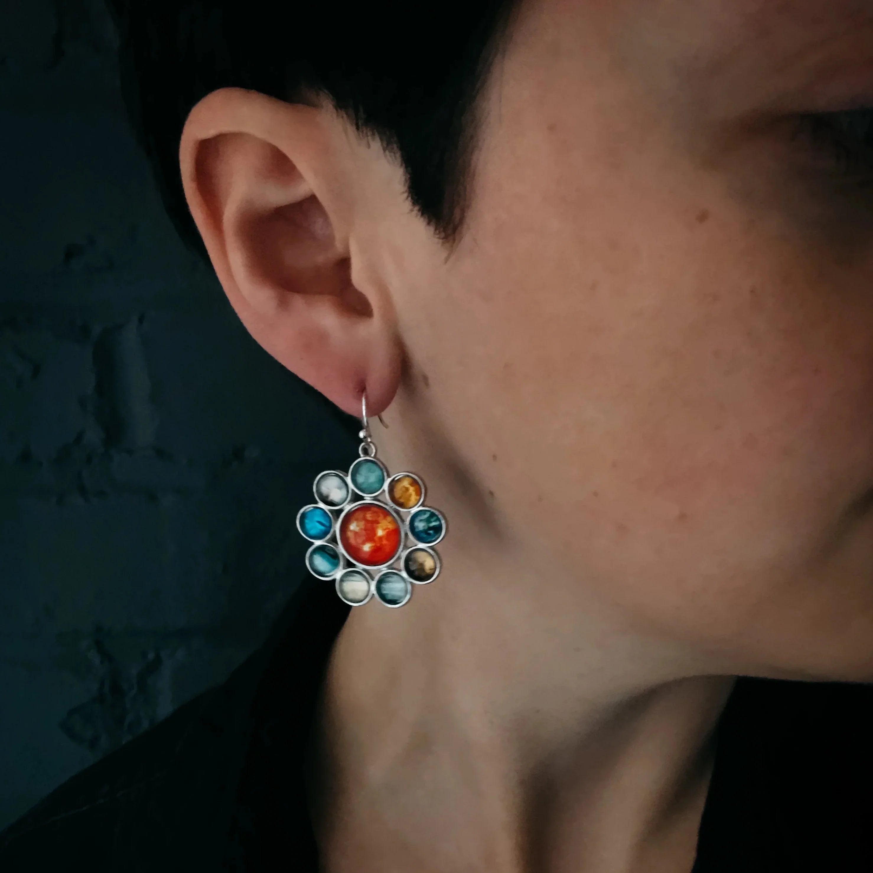 Close-up of ear wearing a solar system planet-themed dangle earring with colorful stones