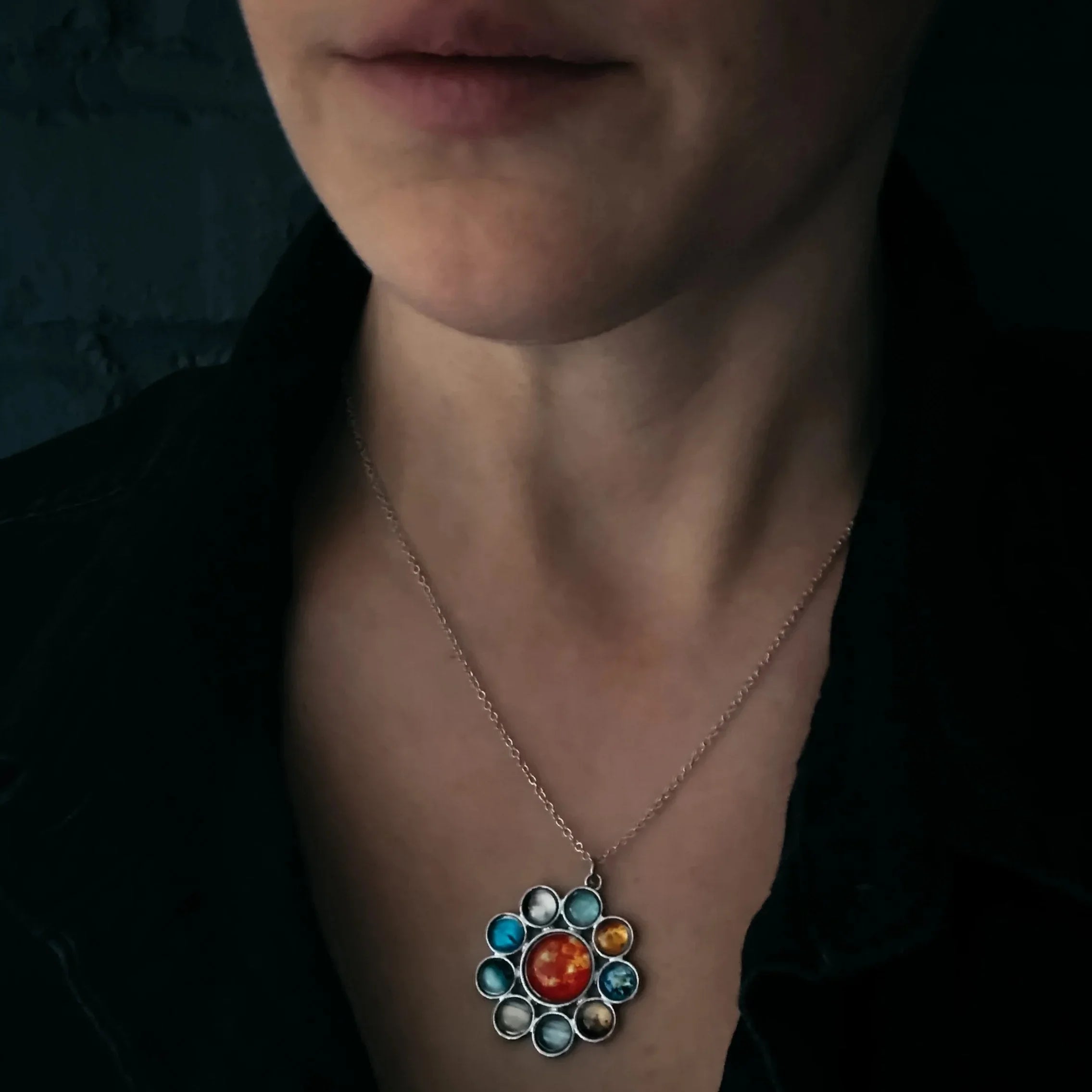 Close-up of a person wearing a silver necklace with solar system planets pendant
