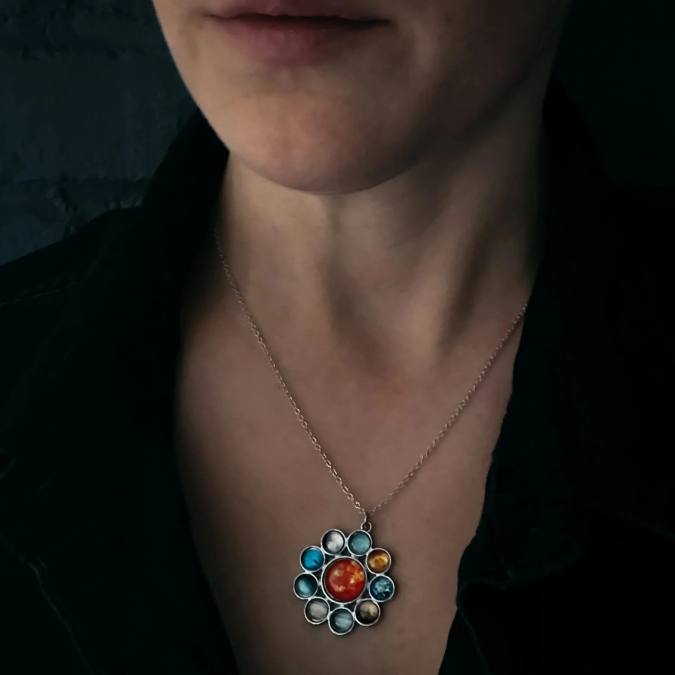 Close-up of a person wearing a silver chain necklace with a colorful solar system pendant