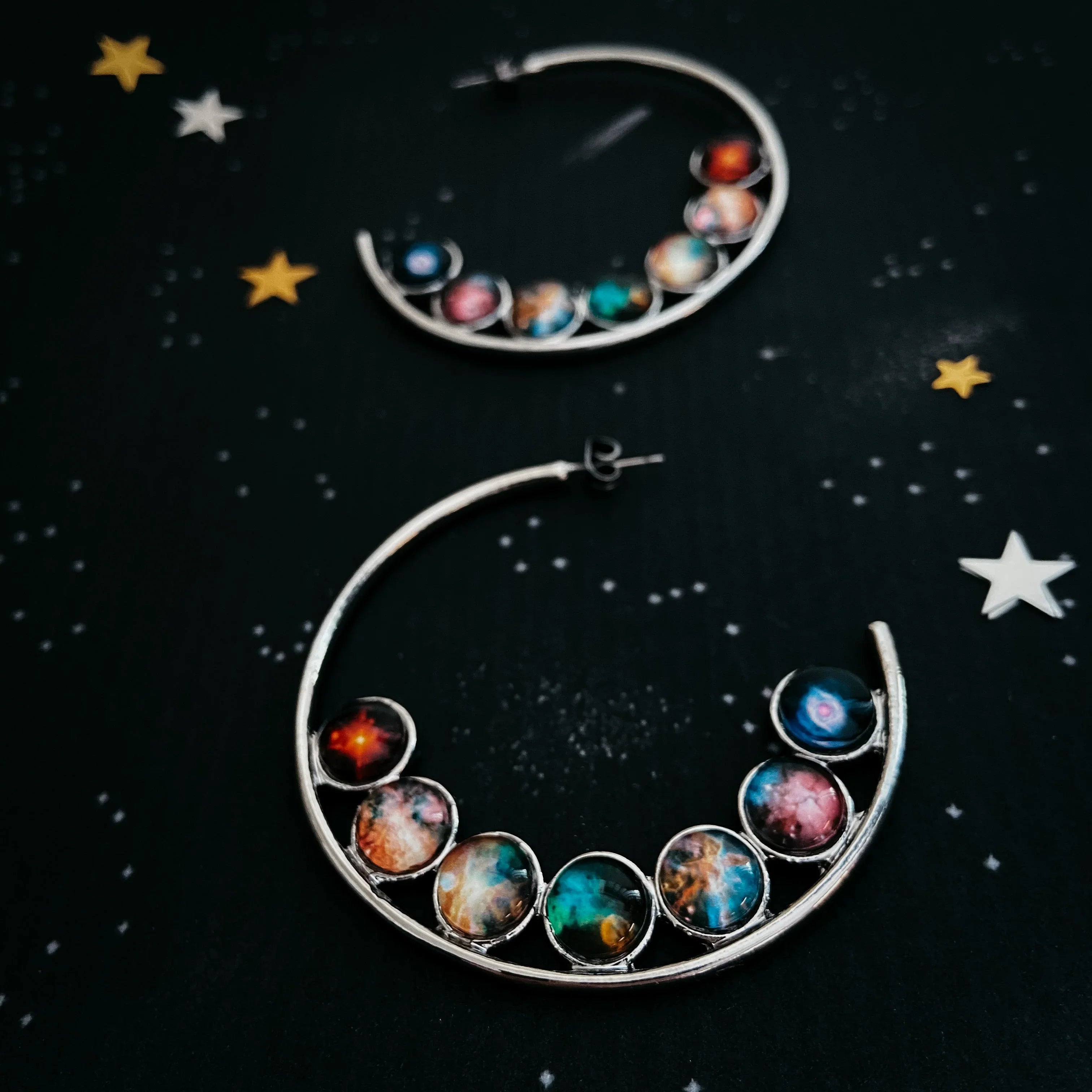 Silver crescent moon earrings with colorful galaxy stone designs on a black starry background