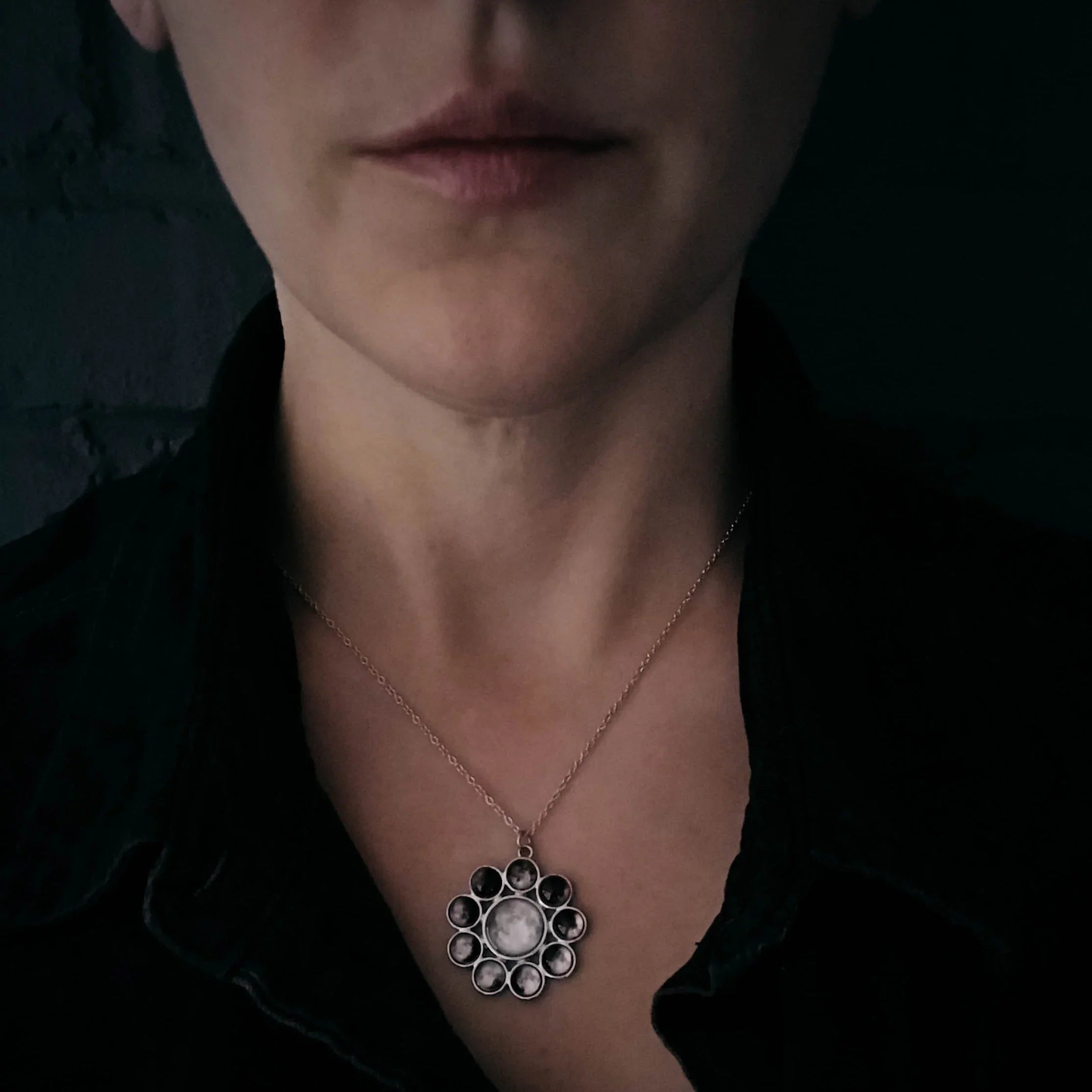Person wearing black shirt with silver moon phase pendant necklace on neck
