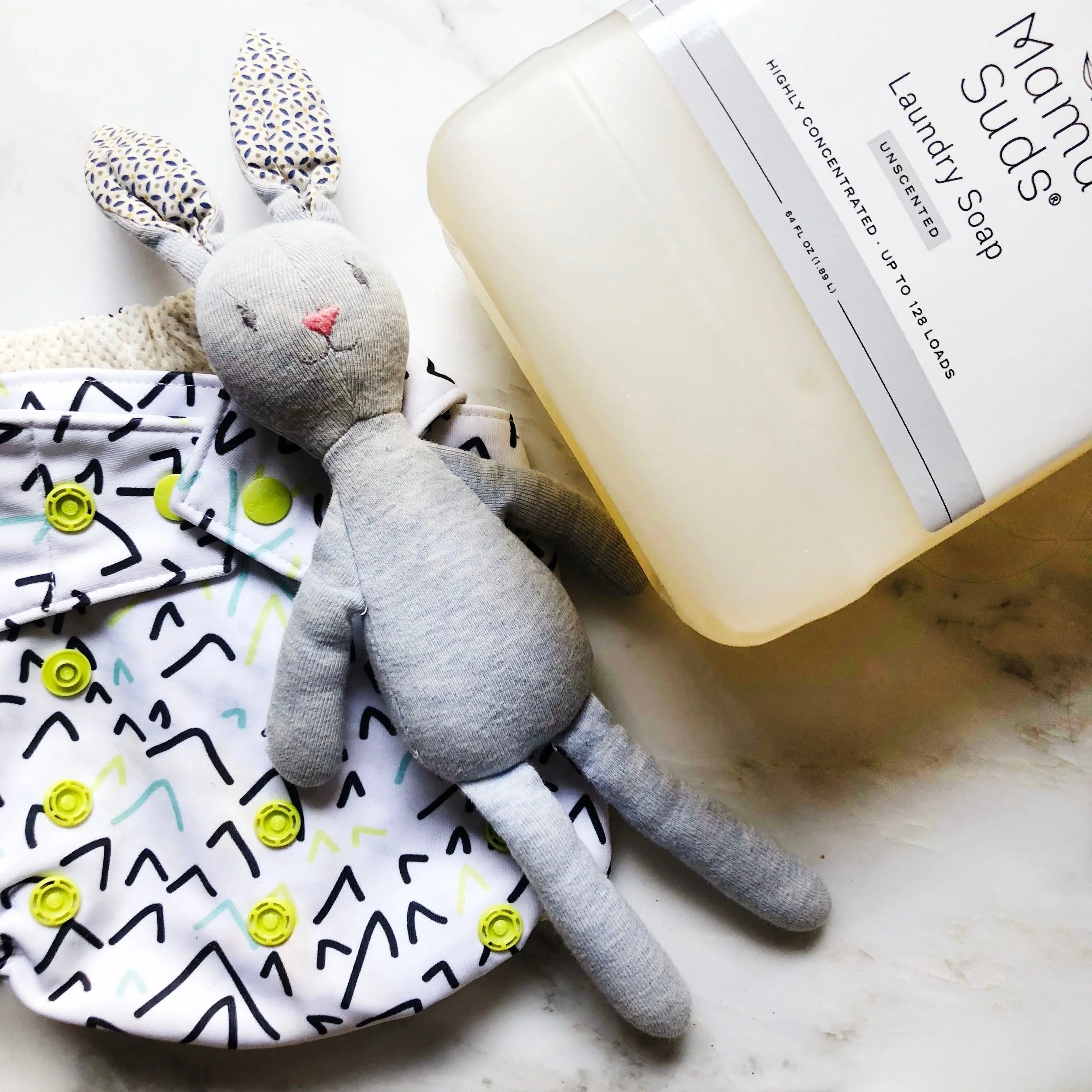 Eco-friendly laundry soap, cloth diaper, and soft bunny plush on marble surface at Qu!rk Boutique