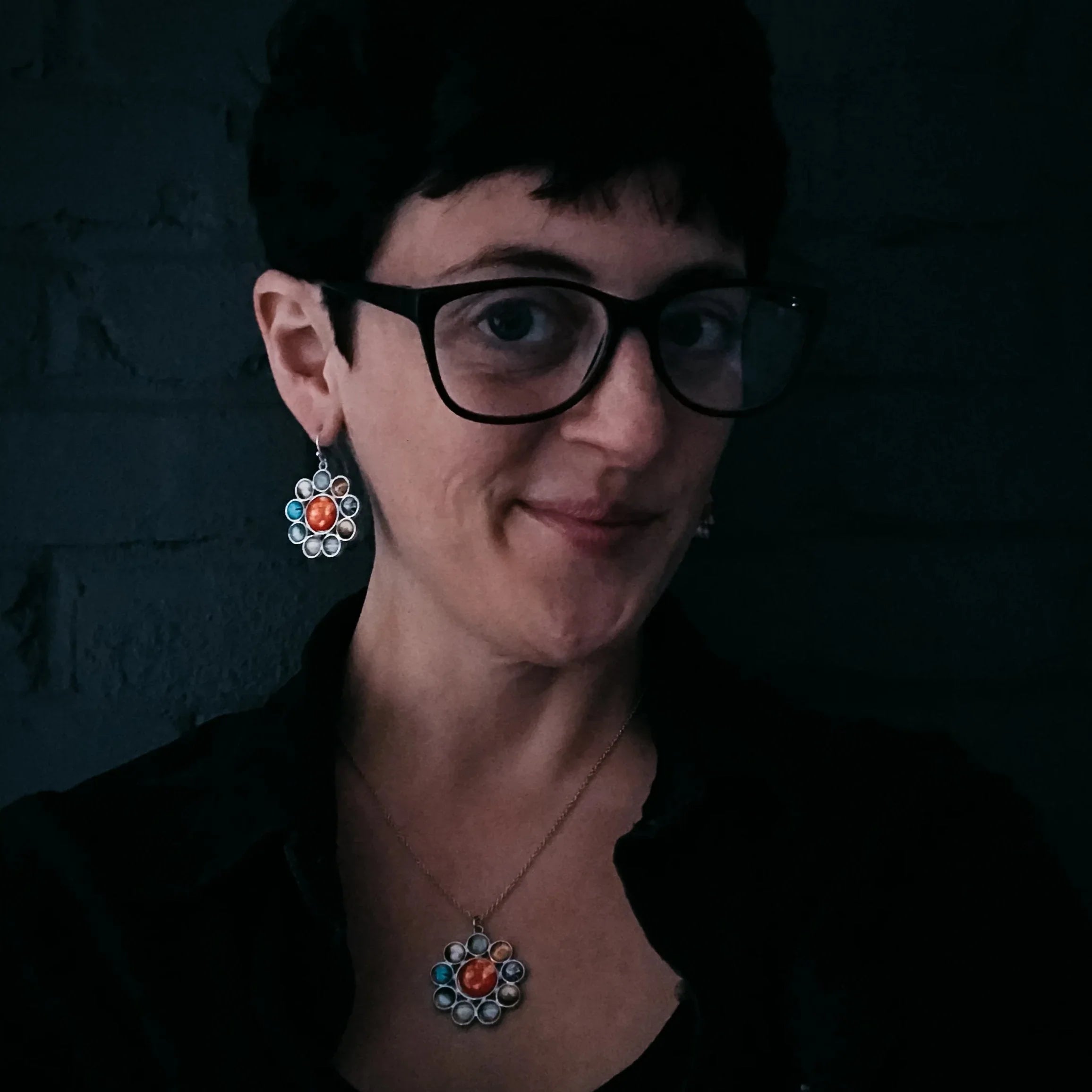 Woman with short dark hair wearing black glasses and colorful stone jewelry necklace and earrings