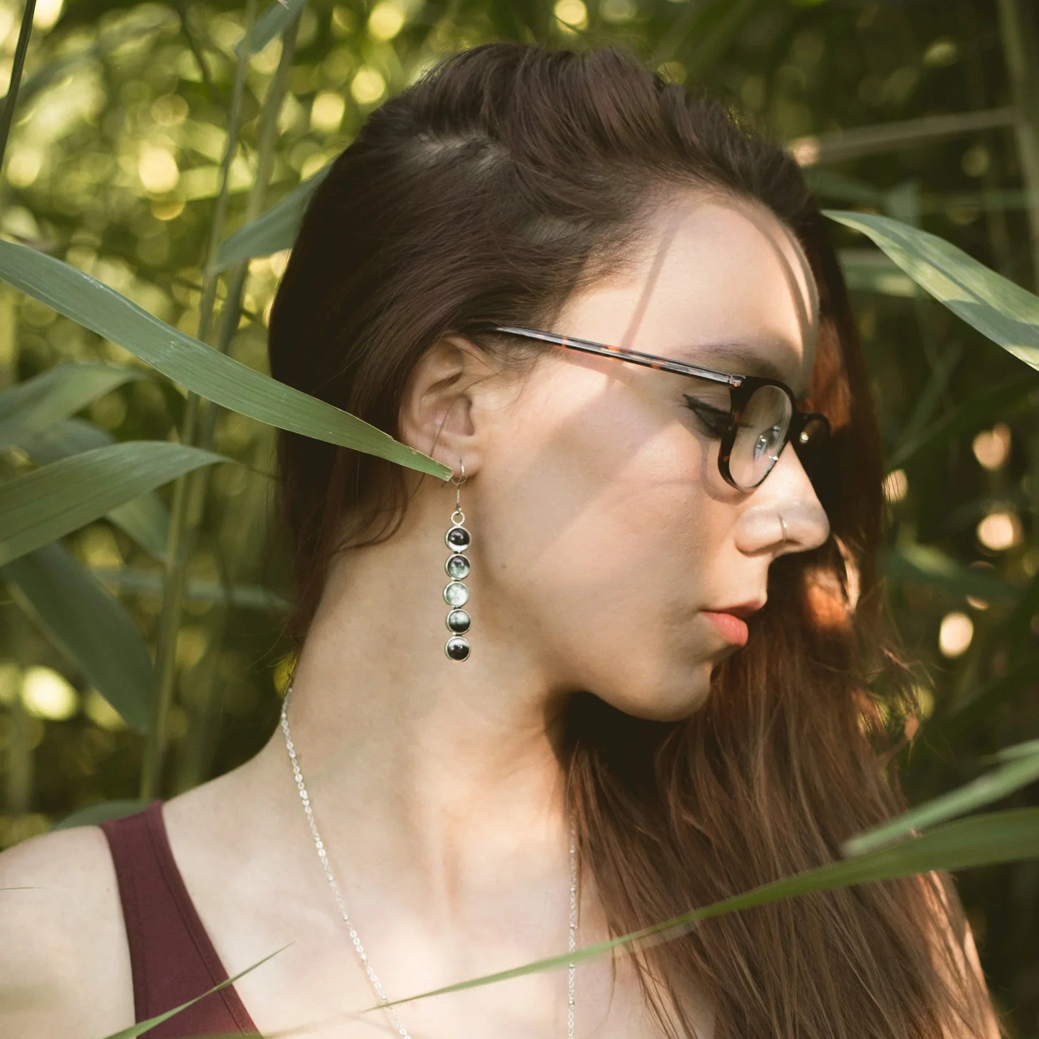 Profile of woman with glasses and long earrings in a natural green outdoor setting