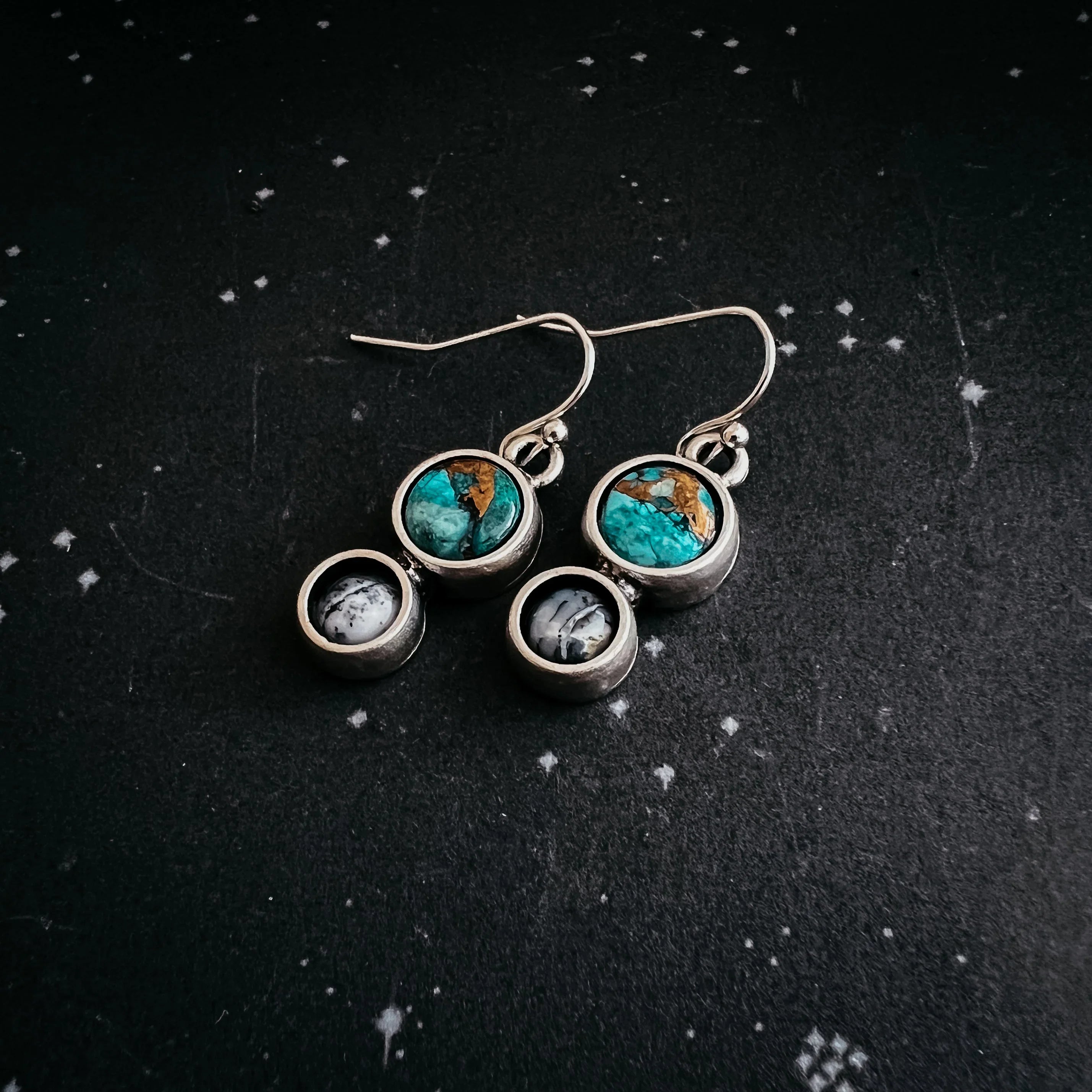 Silver dangle earrings with turquoise and black gemstone accents on black textured background