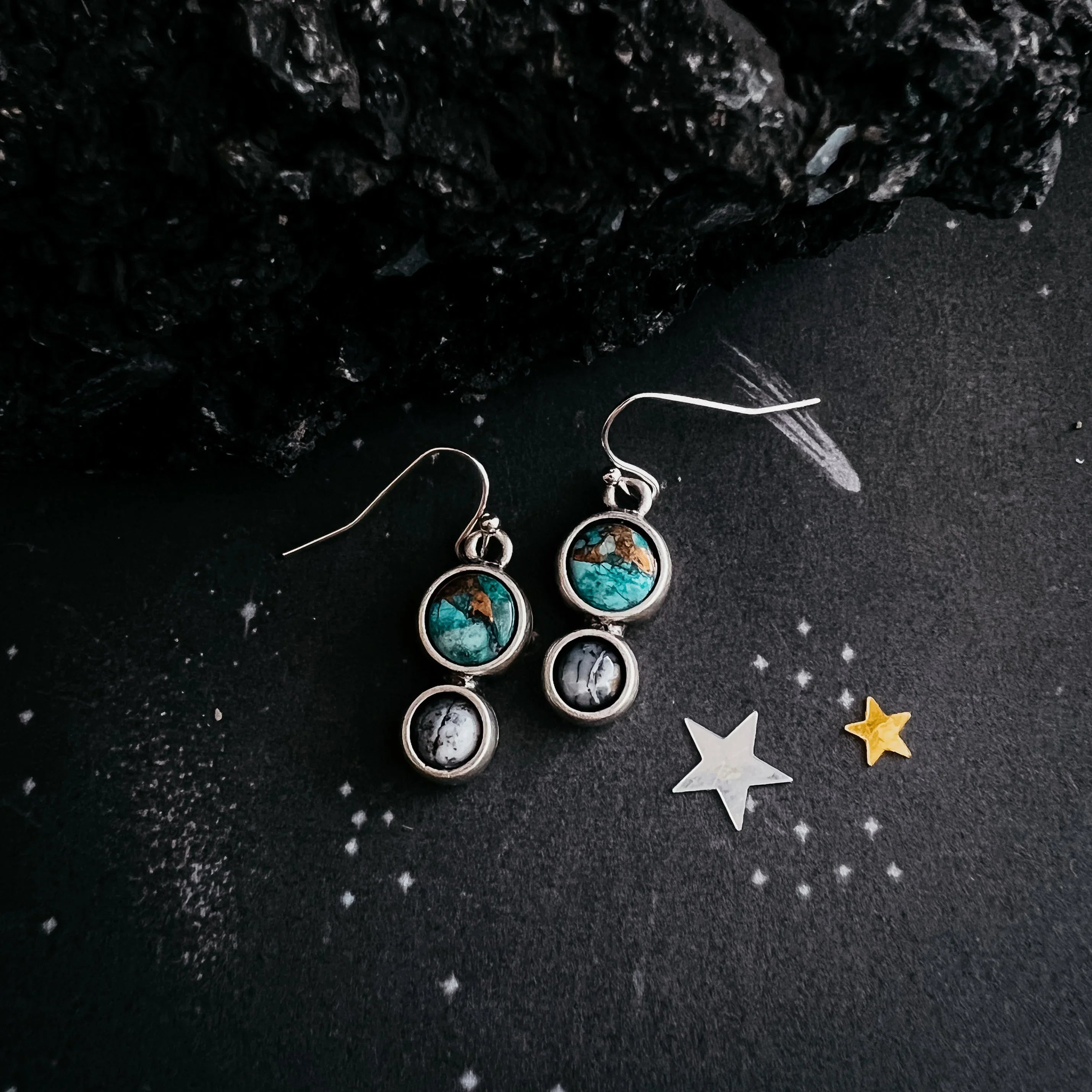 Silver drop earrings with turquoise and black stones, styled on black starry background