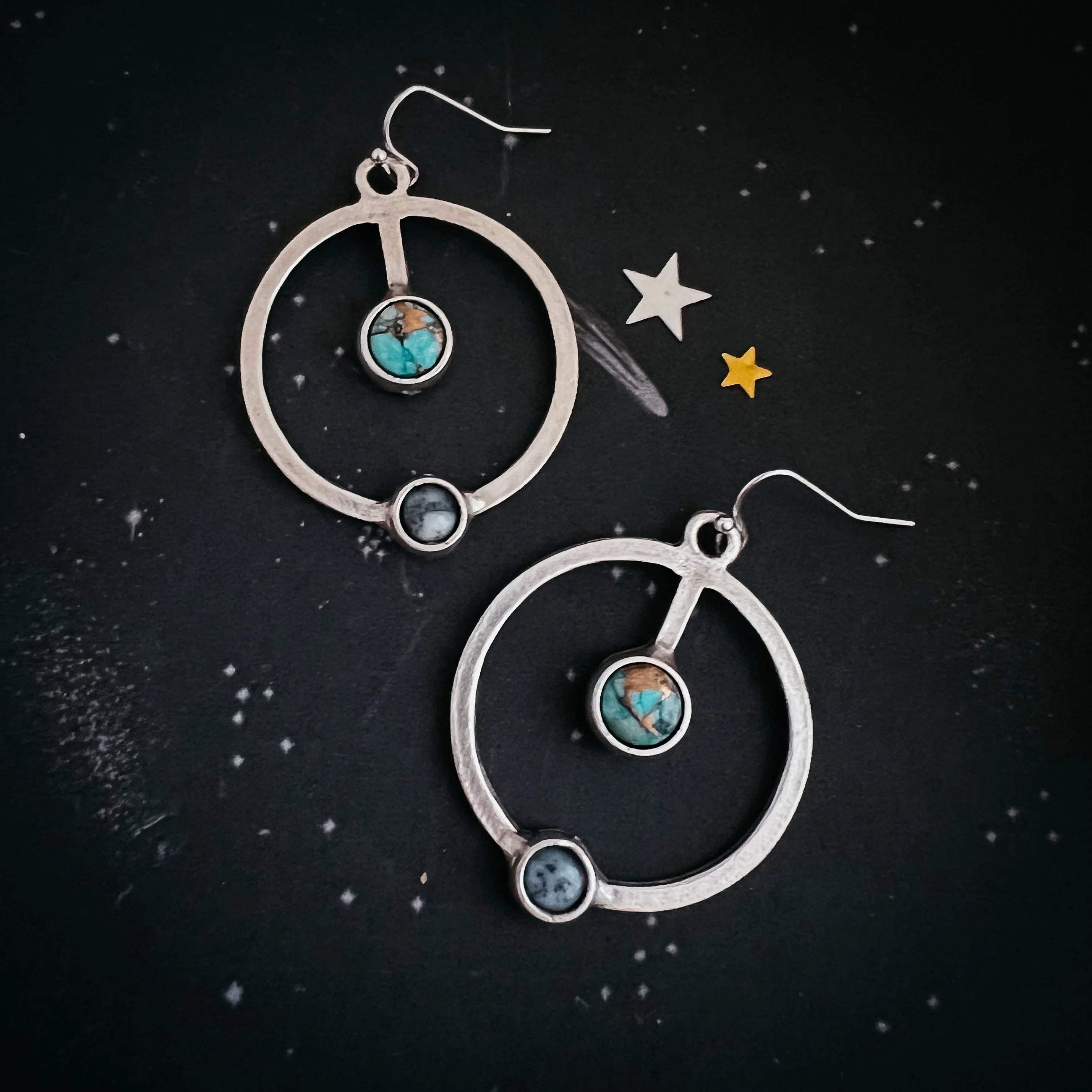 Silver hoop earrings with turquoise and dark round stones on a black starry background