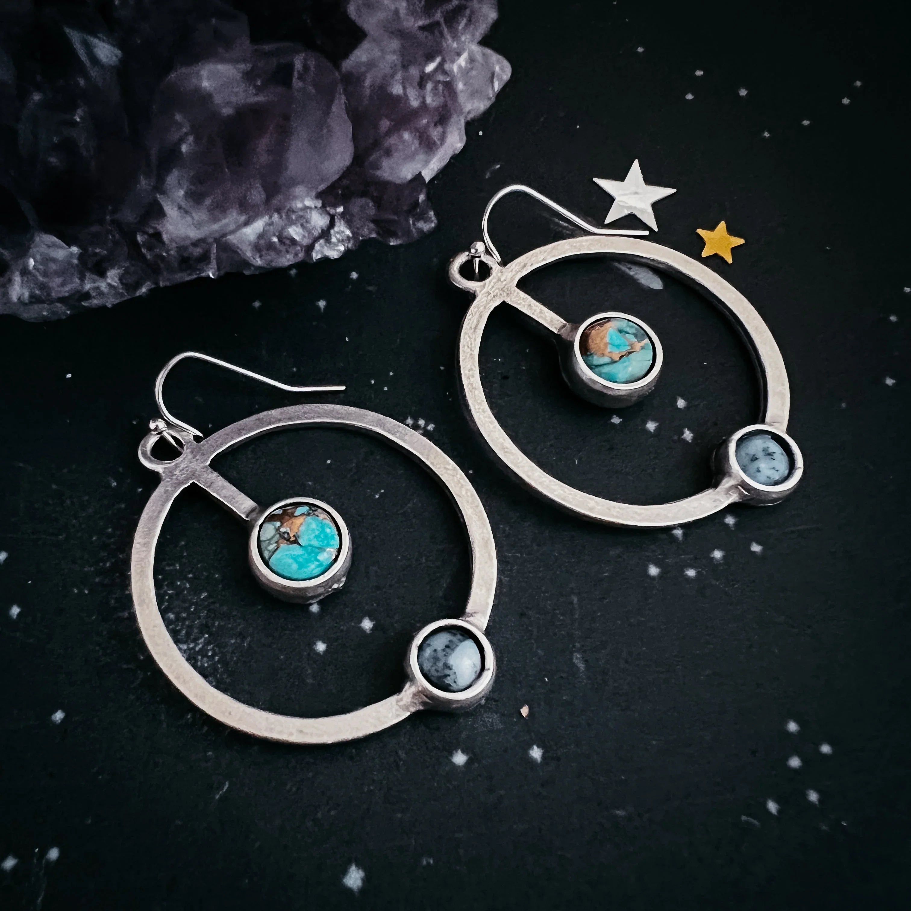 Silver hoop earrings with turquoise and white stone accents on dark starry backdrop with amethyst crystal