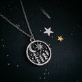 Cosmic-themed silver pendant necklace with trees, stars, and moon, on starry black background