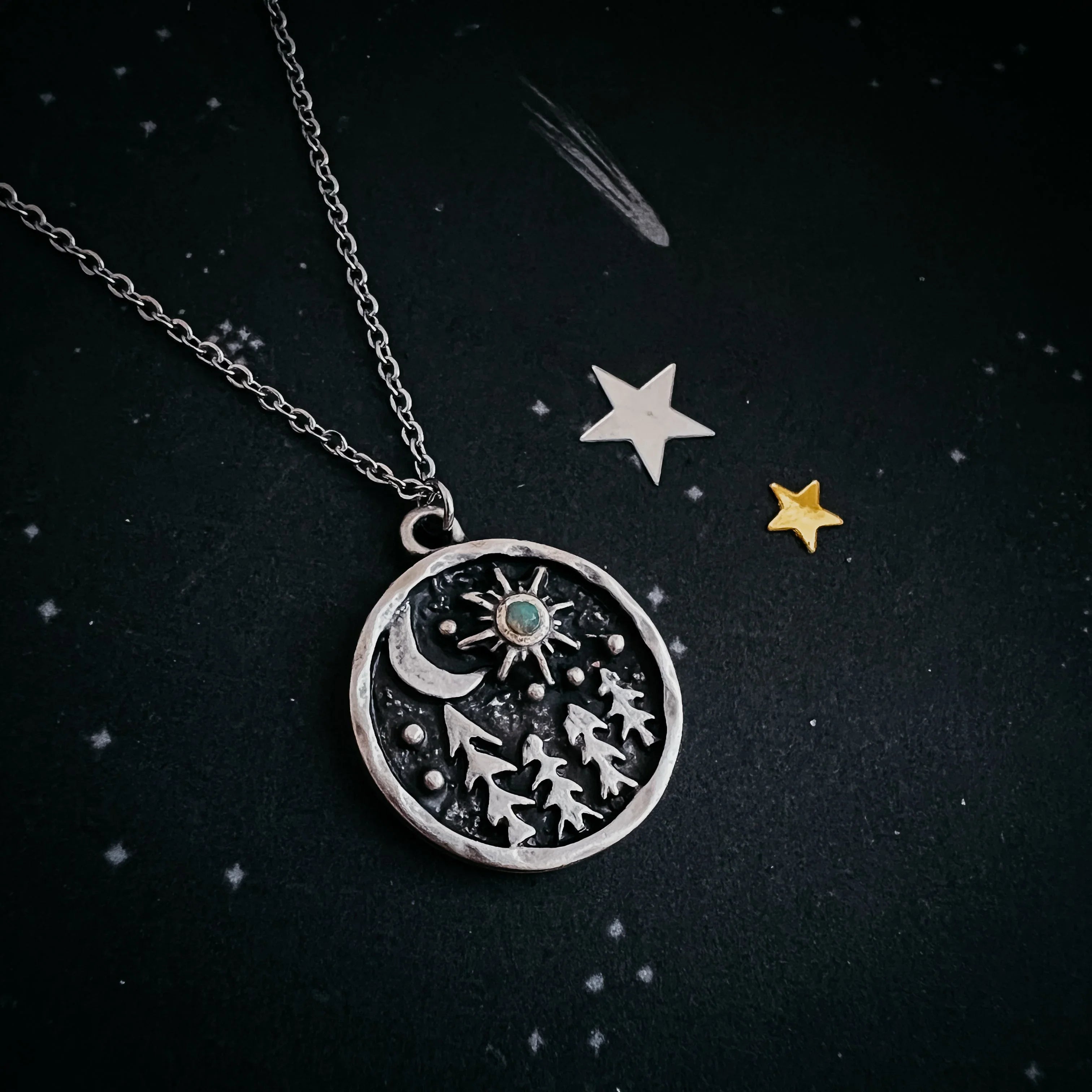 Cosmic-themed silver pendant necklace with trees, stars, and moon, on starry black background