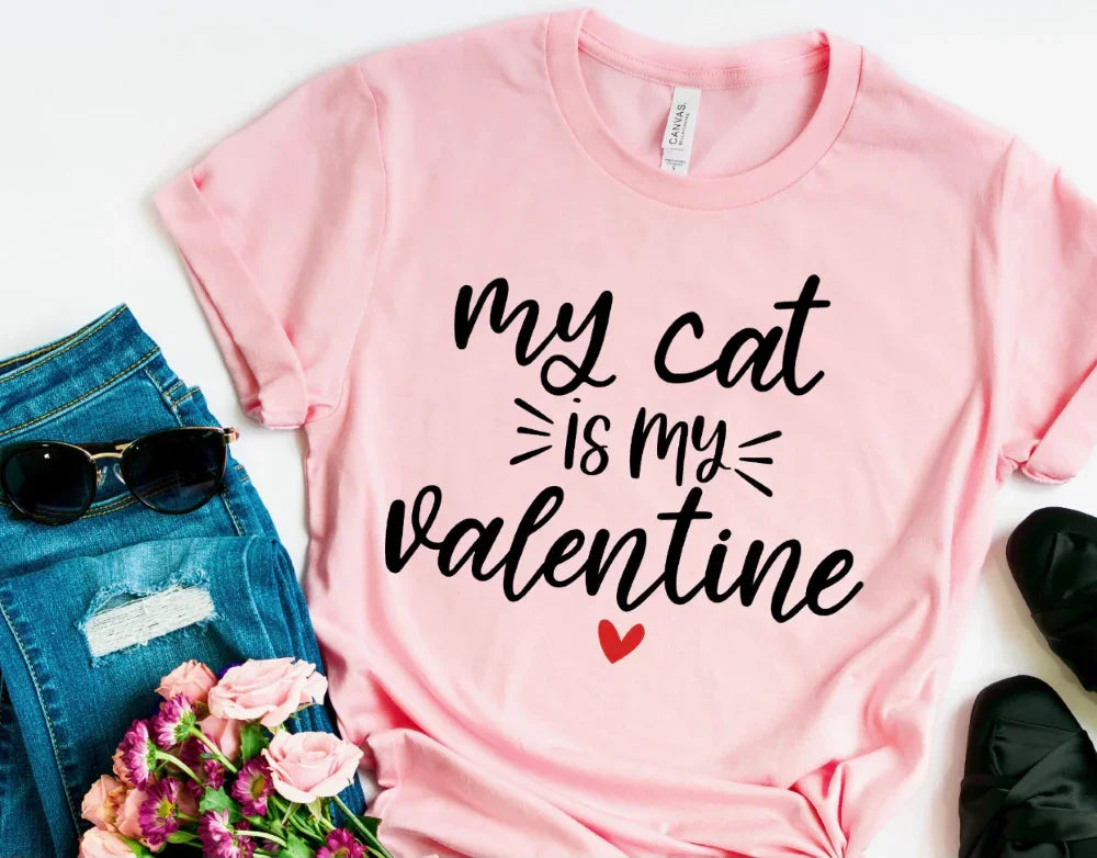 Pink graphic tee with 'my cat is my valentine' text, styled with jeans, flowers, and sunglasses
