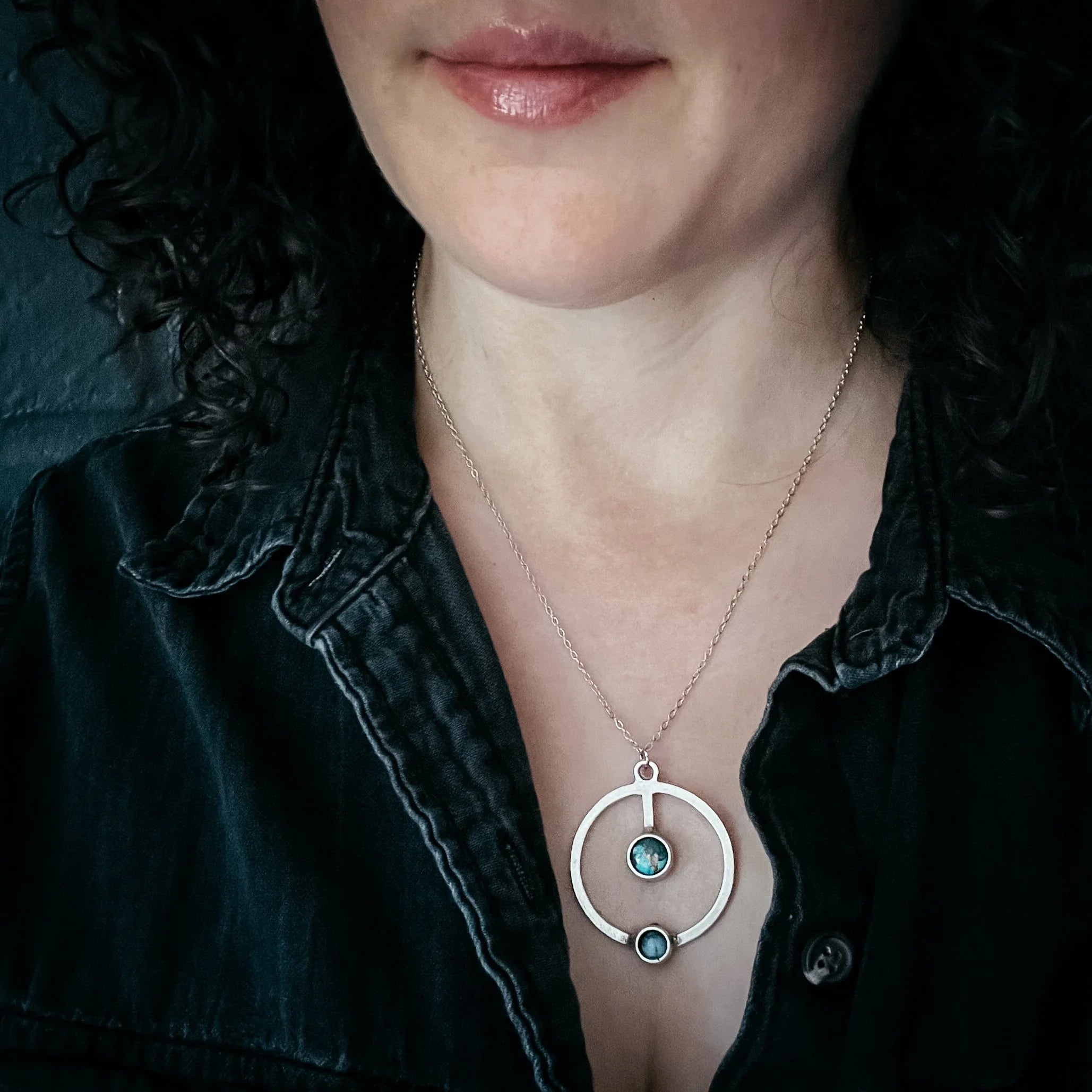 Woman wearing modern silver pendant necklace with blue stones and black shirt