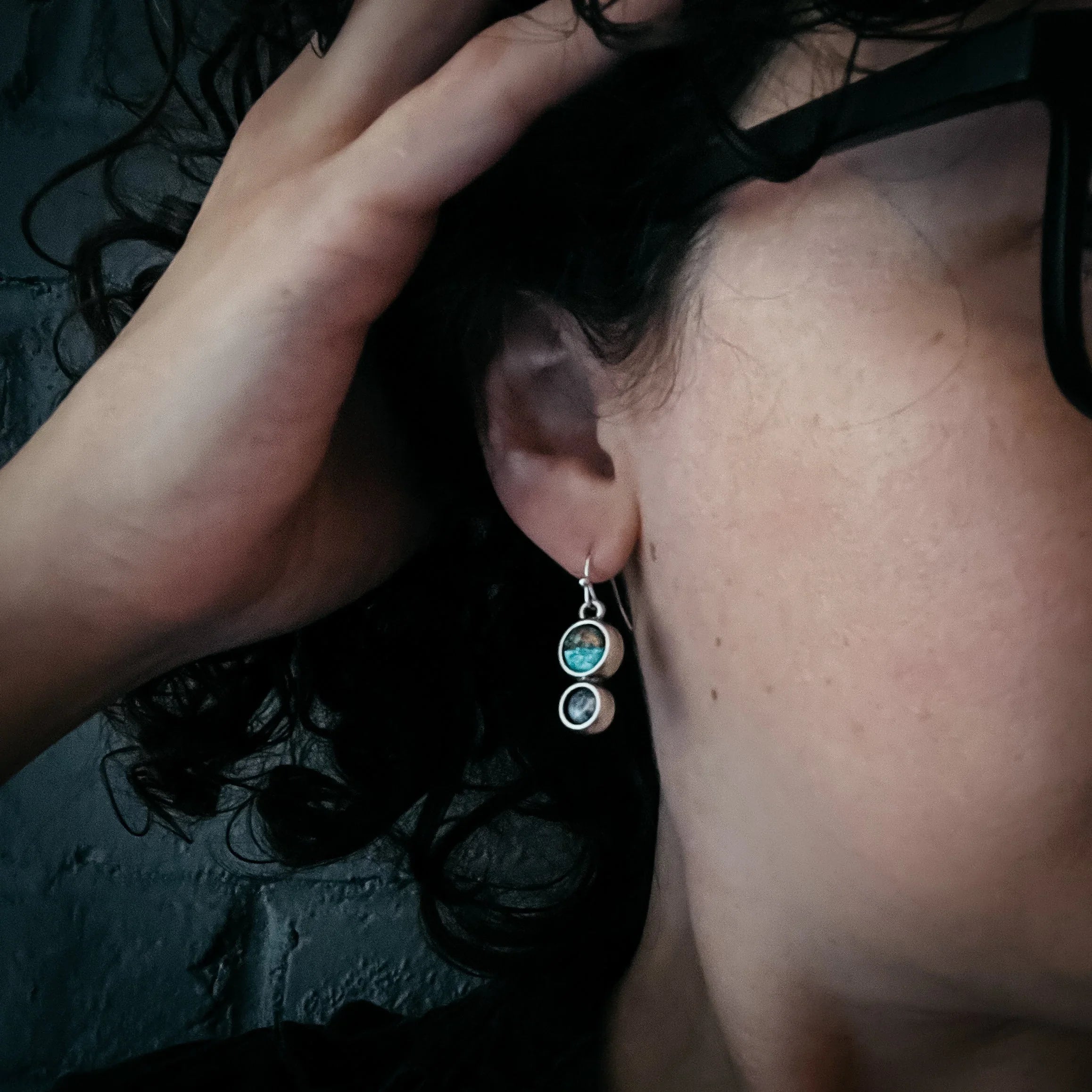 Close-up of woman wearing unique handmade turquoise and silver drop earrings with curly black hair