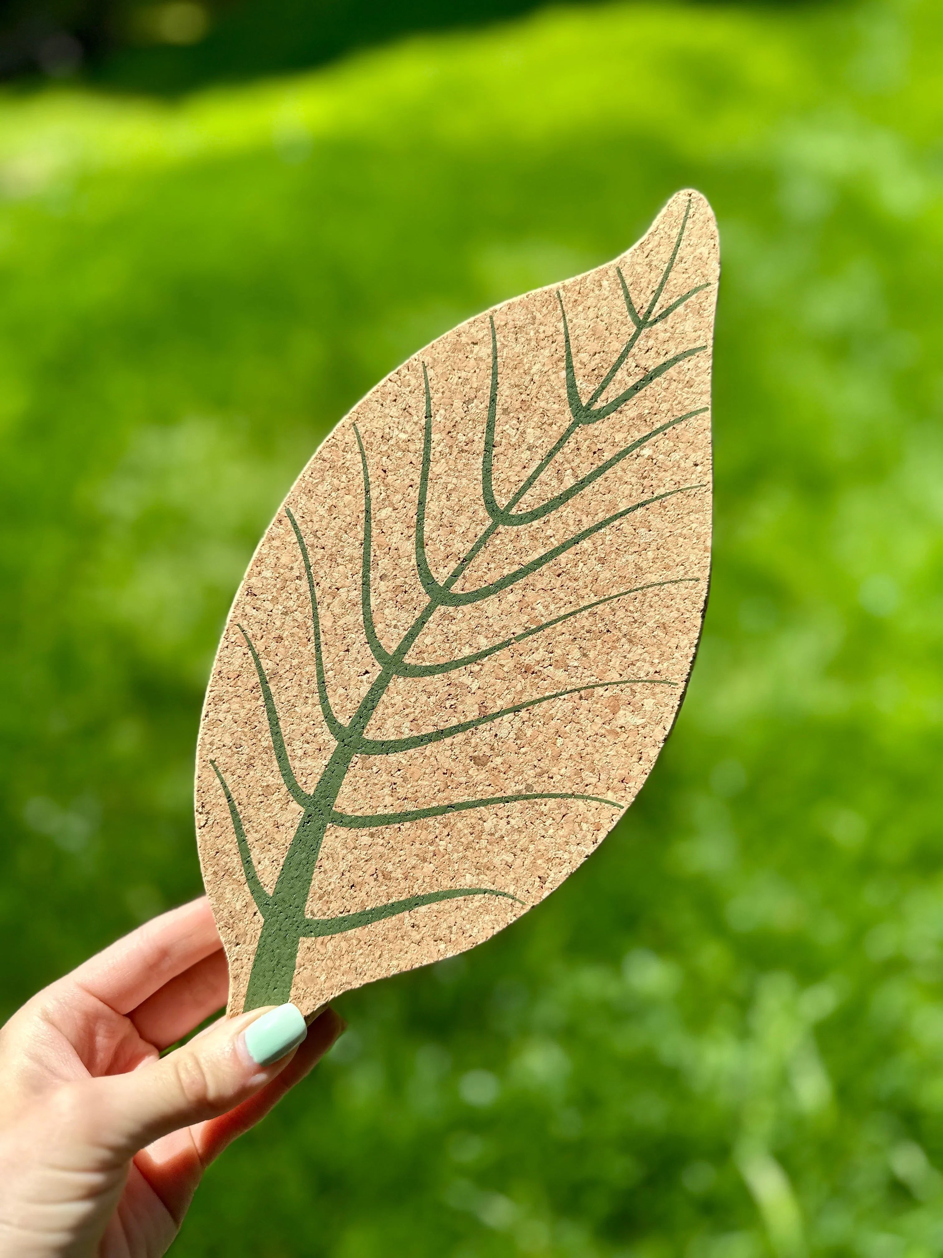 Hand holding a cork leaf-shaped trivet with green vein design, eco-friendly gift from Qu!rk Boutique