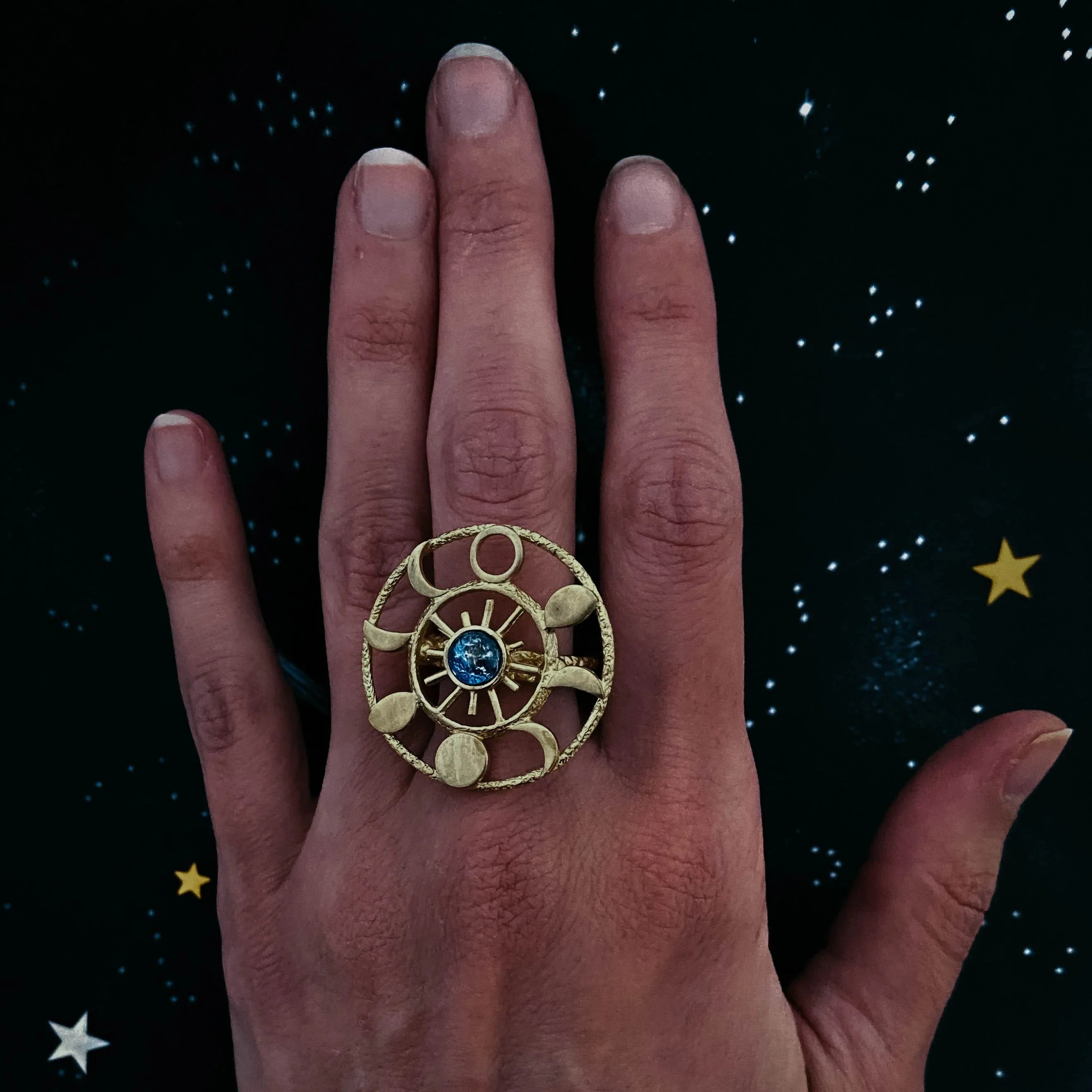 Hand wearing a gold zodiac-themed ring with a blue stone on starry night background