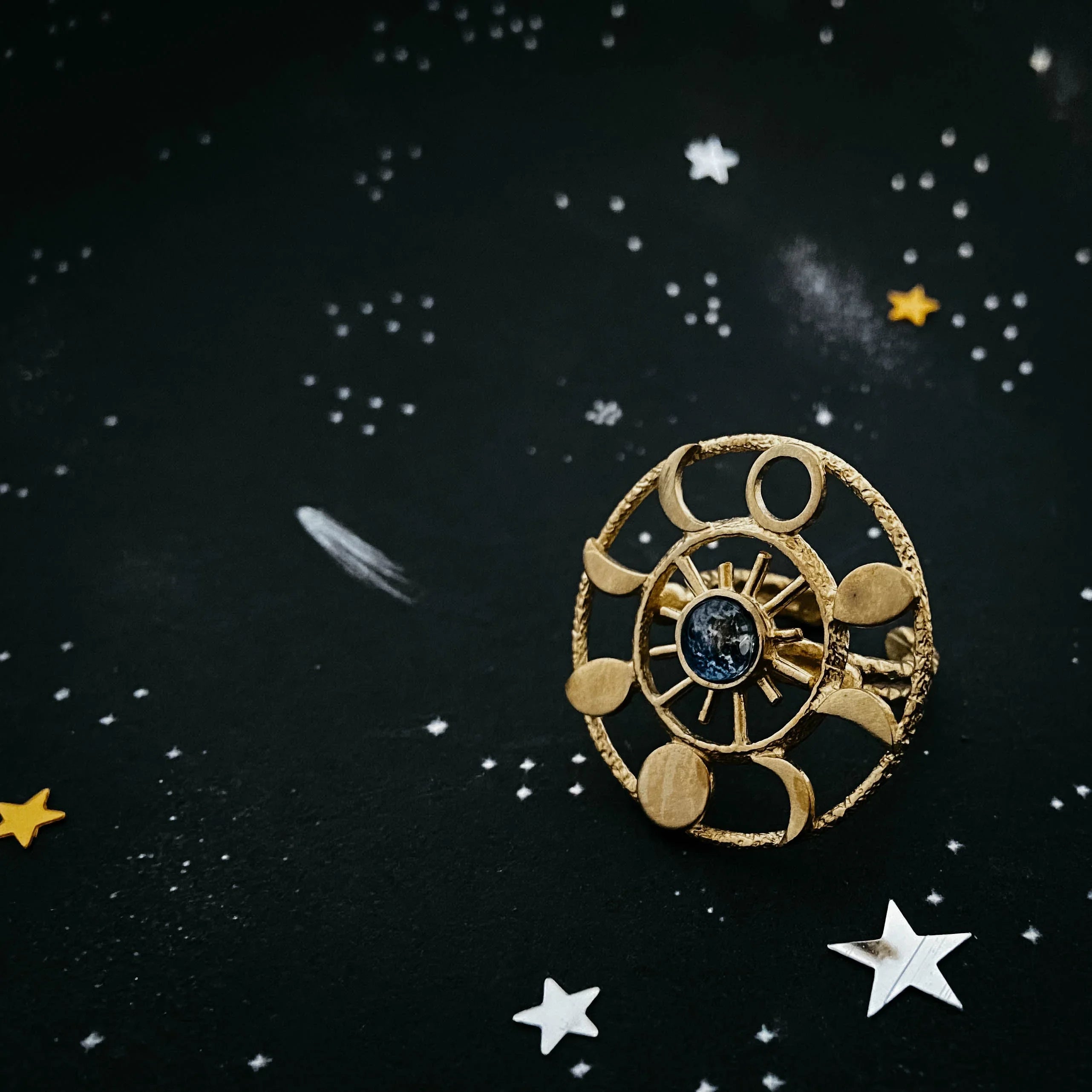 Gold celestial ring with moon phases and a blue gemstone on starry black background